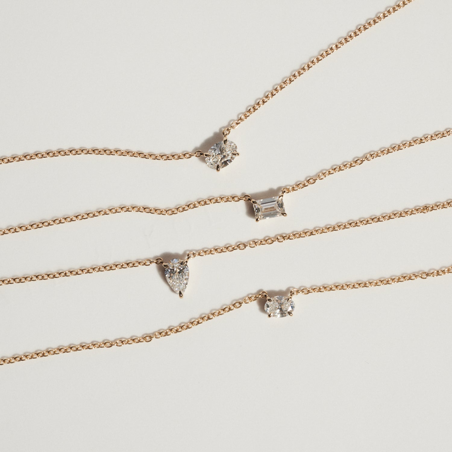 Set of gold necklaces with various diamond pendants on a light gray background