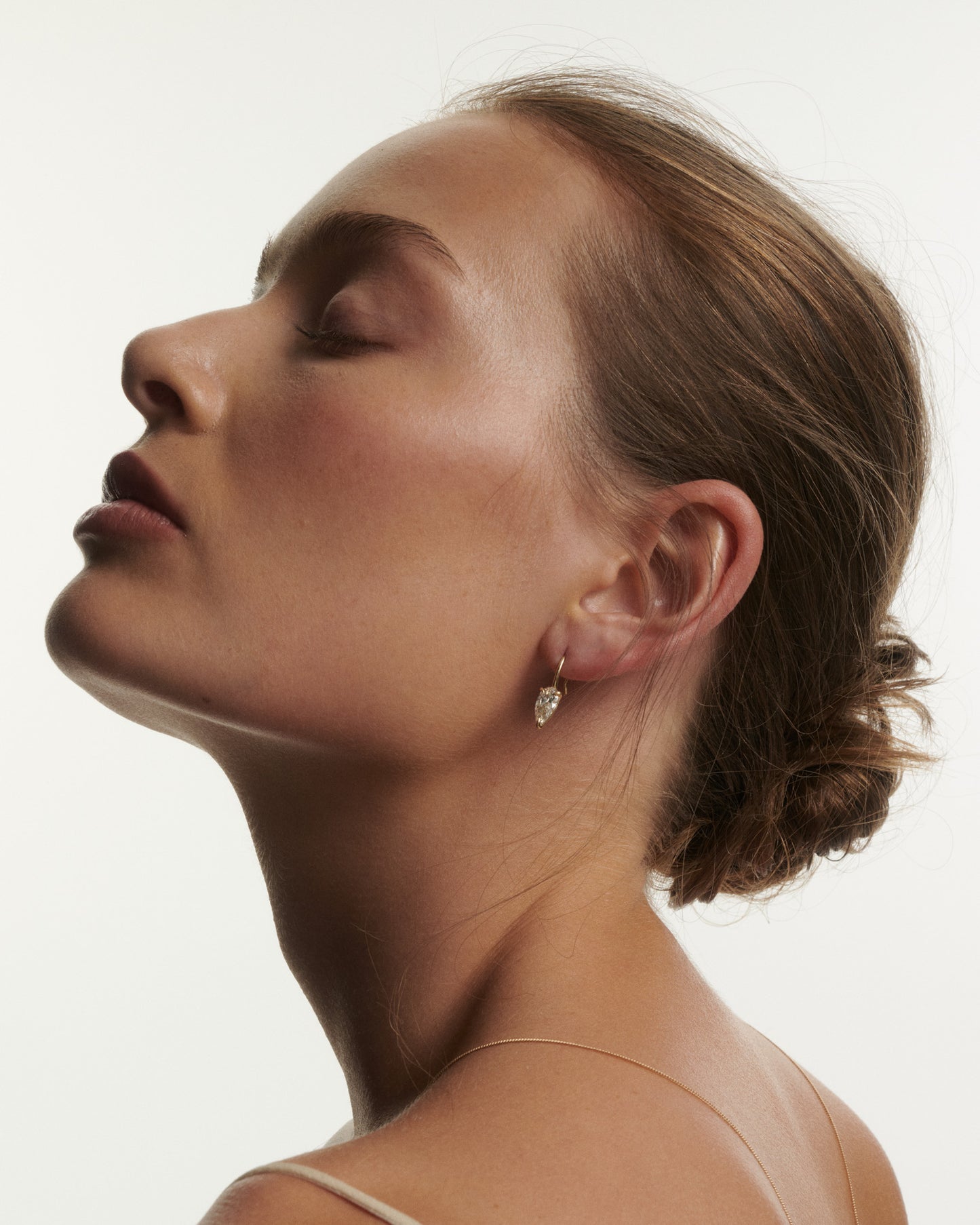 Woman with a bun and diamond earring on a plain background