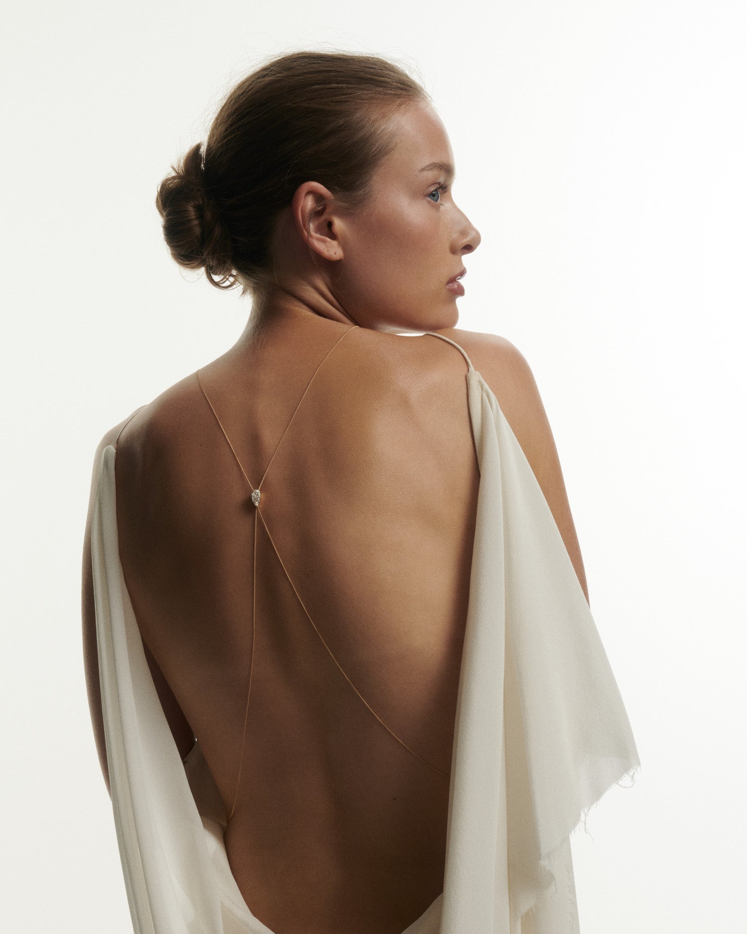 Woman wearing a white dress with thin straps, standing against a plain background