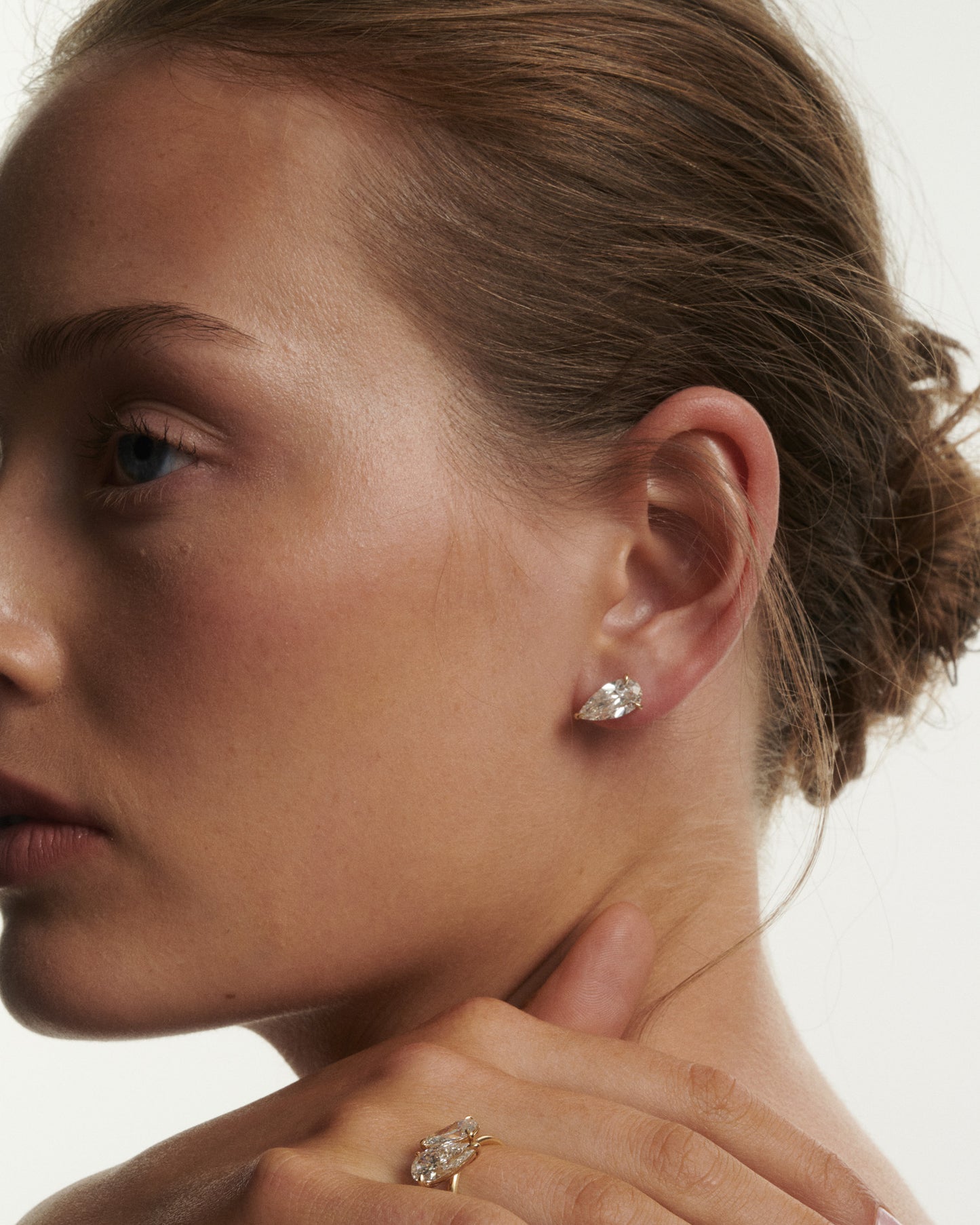 Close-up of a woman wearing diamond earrings and a ring on a neutral background