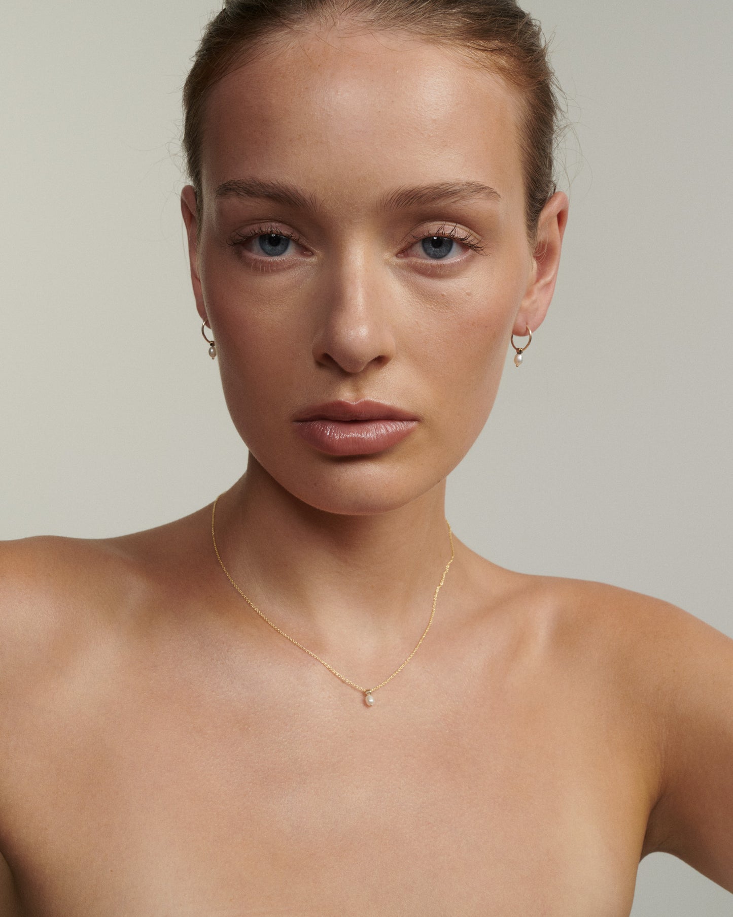 Woman wearing a gold necklace and earrings against a neutral background