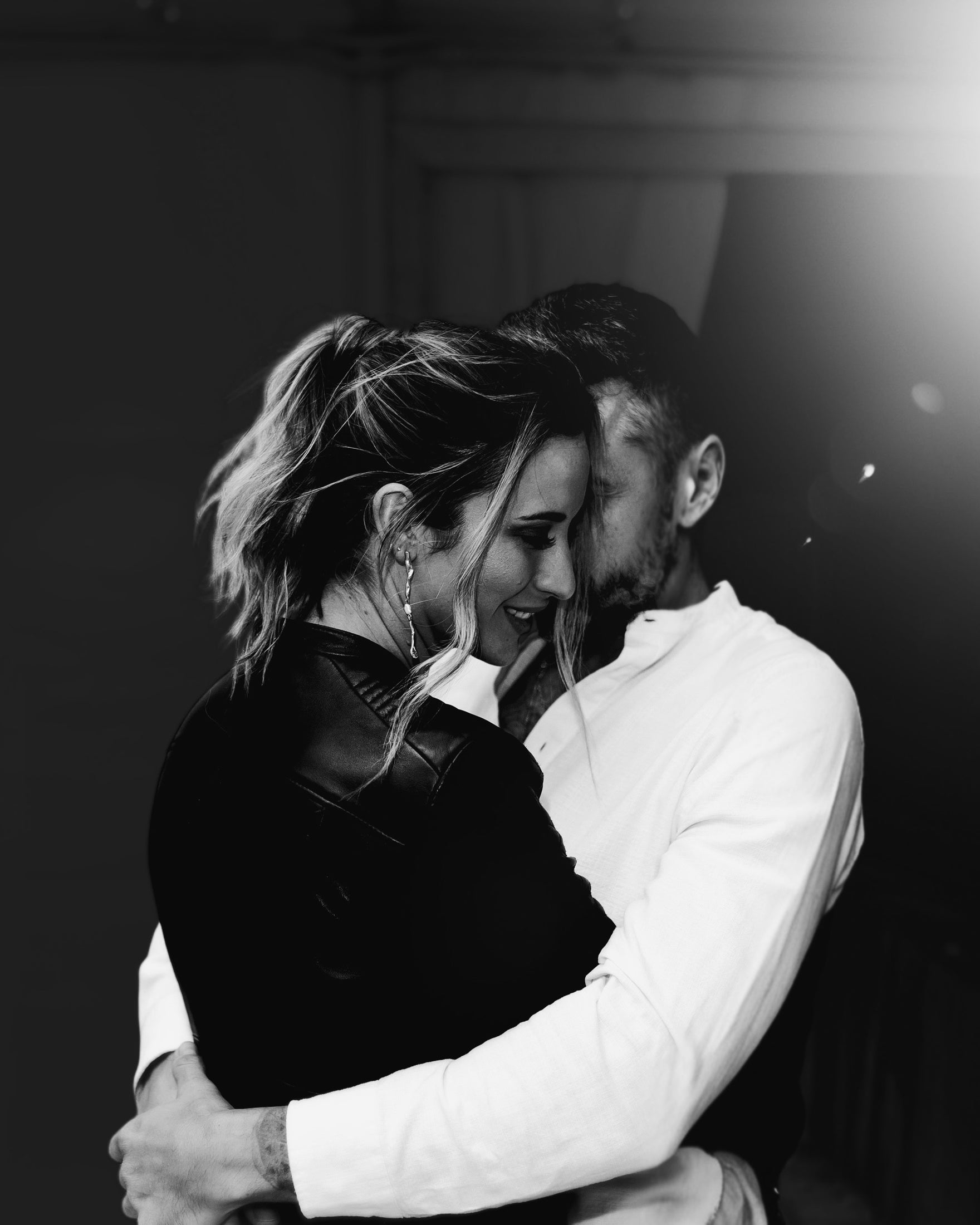 Couple embraces tenderly in monochrome; woman wears elegant hoop earrings, suggesting luxury jewellery. Romantic, intimate scene.