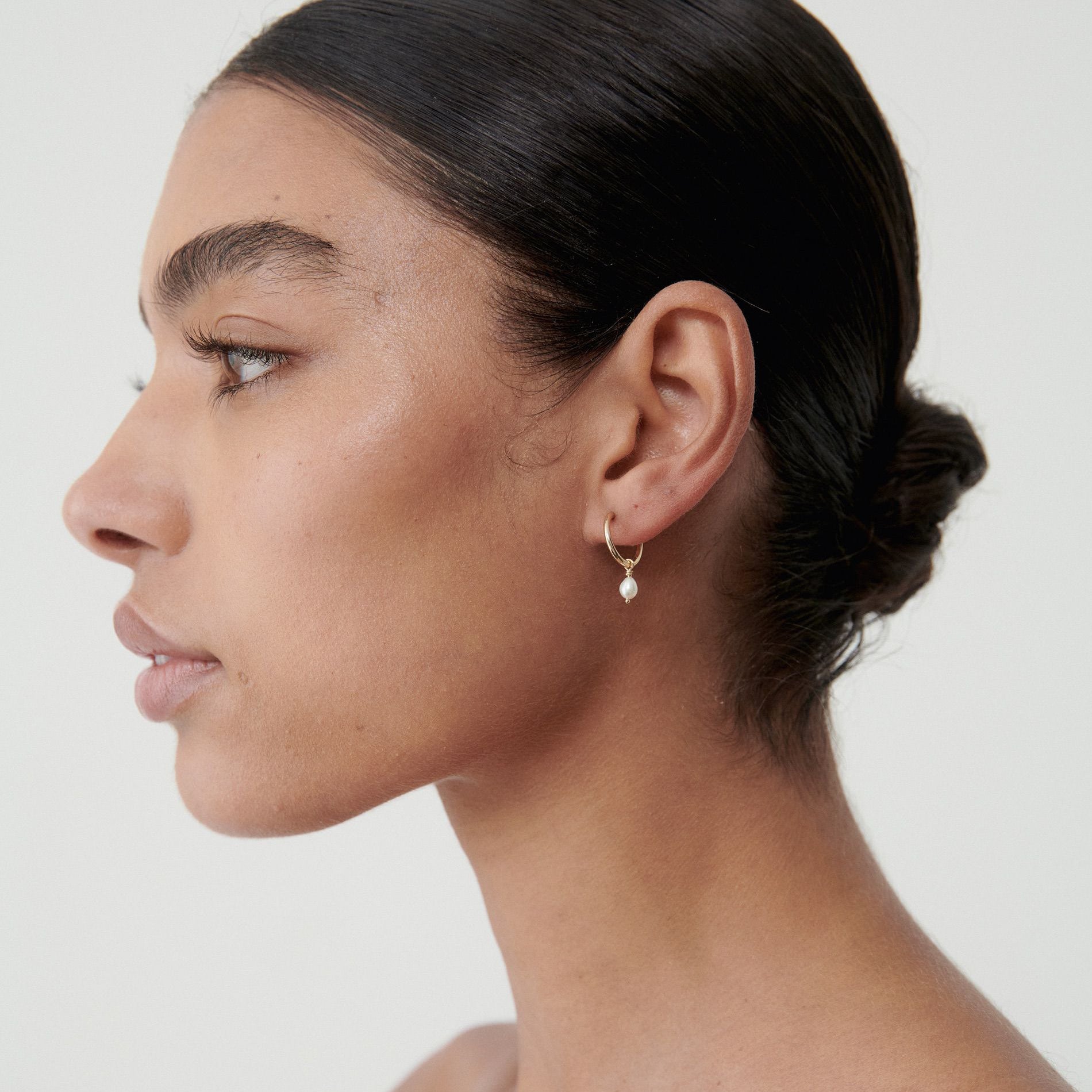 Woman wearing elegant gold dangling earrings with hair in a sleek bun. Minimalist luxury jewellery on a neutral background.