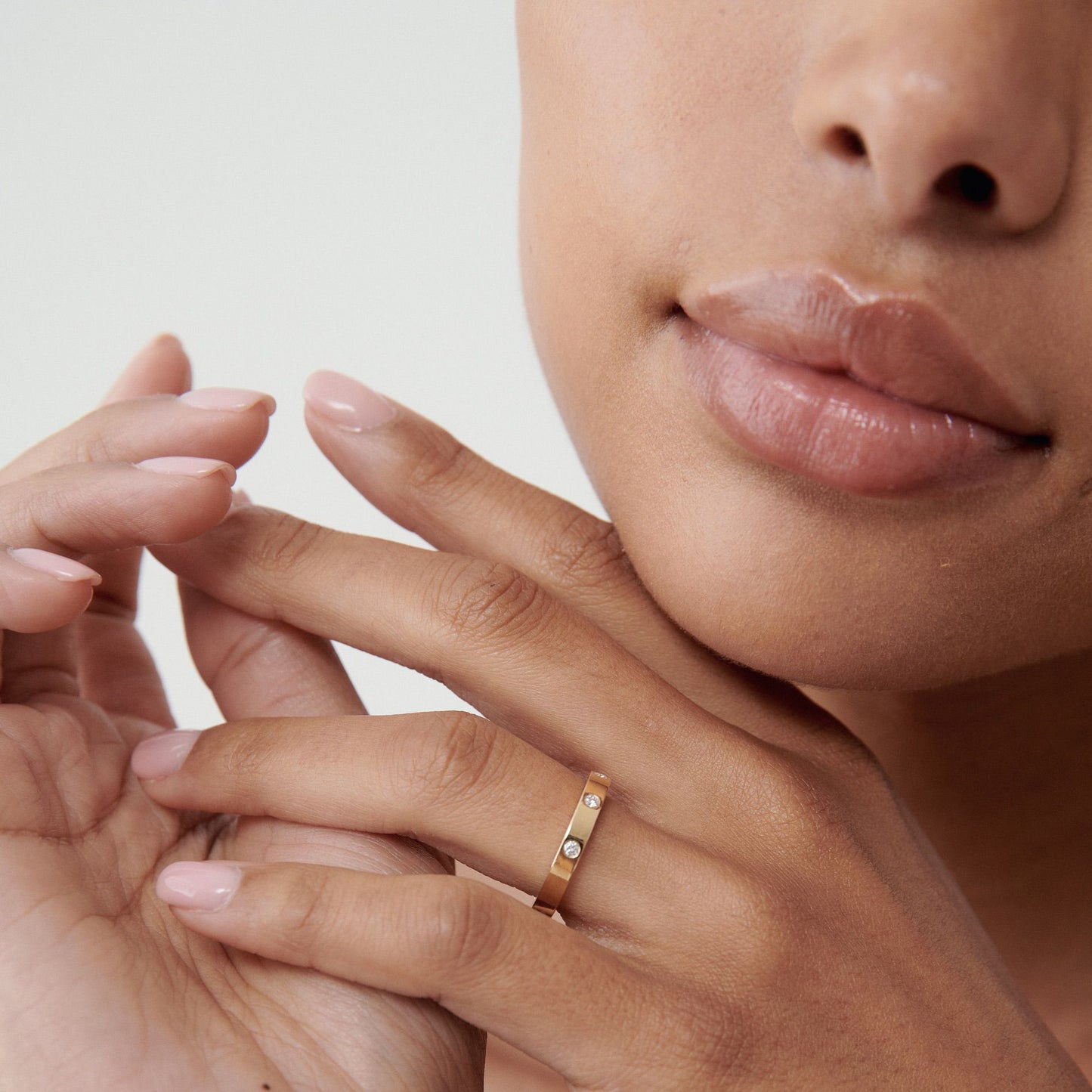 Close-up of a woman's hand wearing a gold diamond ring. Her other hand gently touches the ring. Her lips and chin are visible in soft focus.