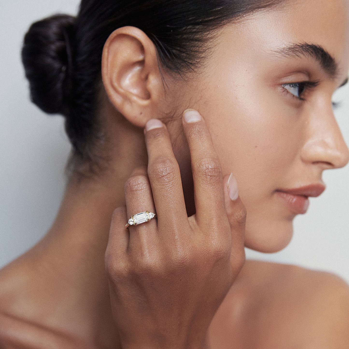 Woman wearing an elegant diamond ring, touching her face. Natural makeup and slicked-back hairstyle; luxury jewellery in focus.