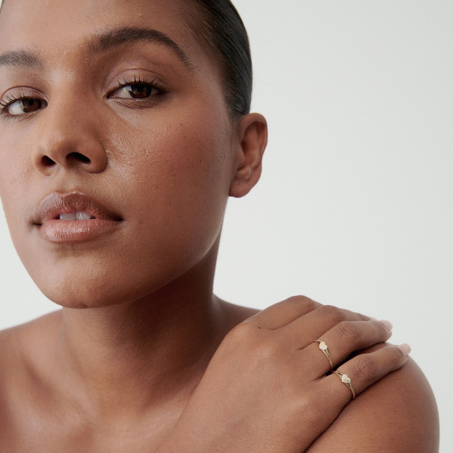 Woman with sleek hair wearing delicate gold rings with small gemstones, posing against a neutral background. Luxury jewellery focus.