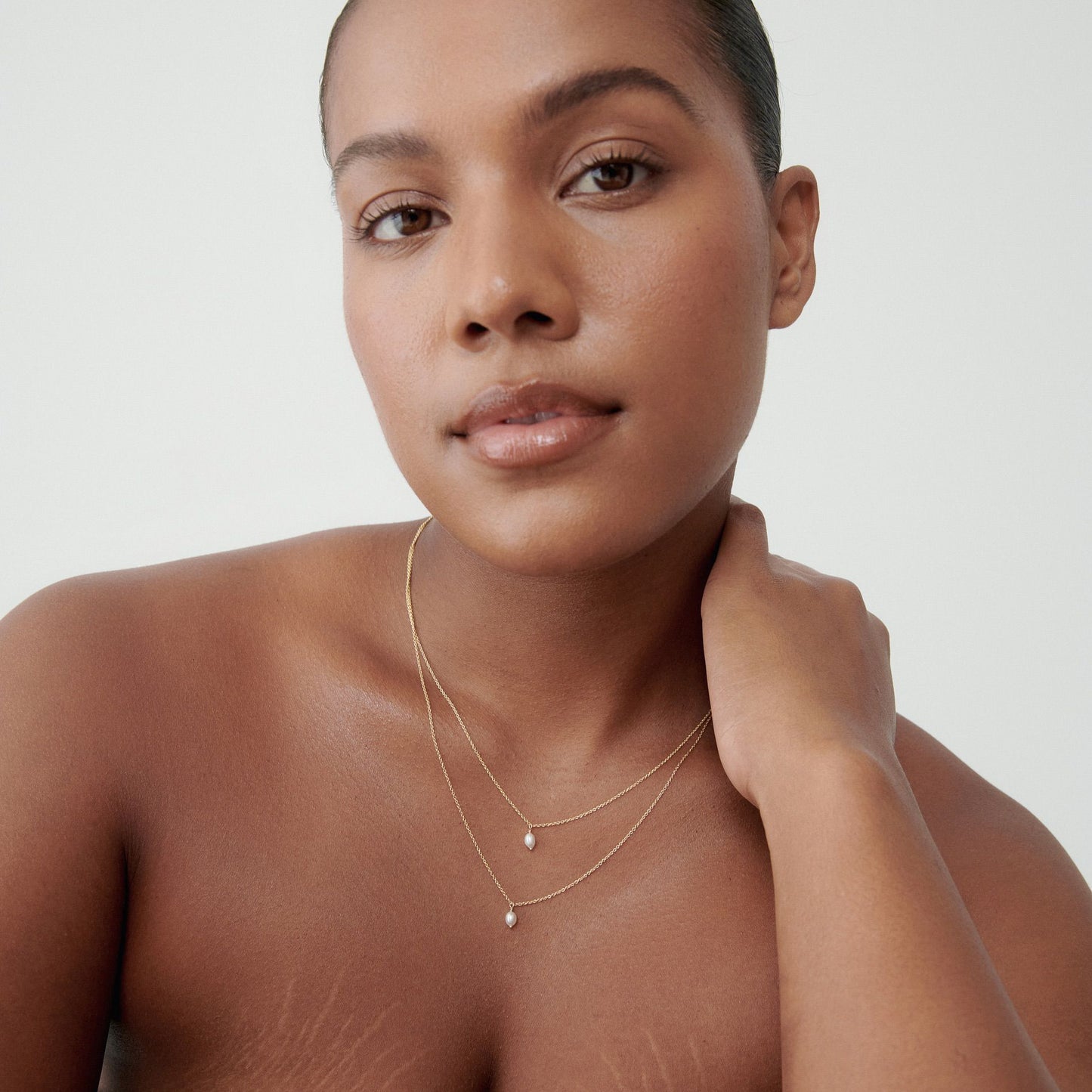 Woman wearing layered gold necklaces with small pearl details, set against a plain background. Elegant jewellery for a luxury look. [text overlay: Model wears 45cm (top) and 50cm (bottom) custom length] 