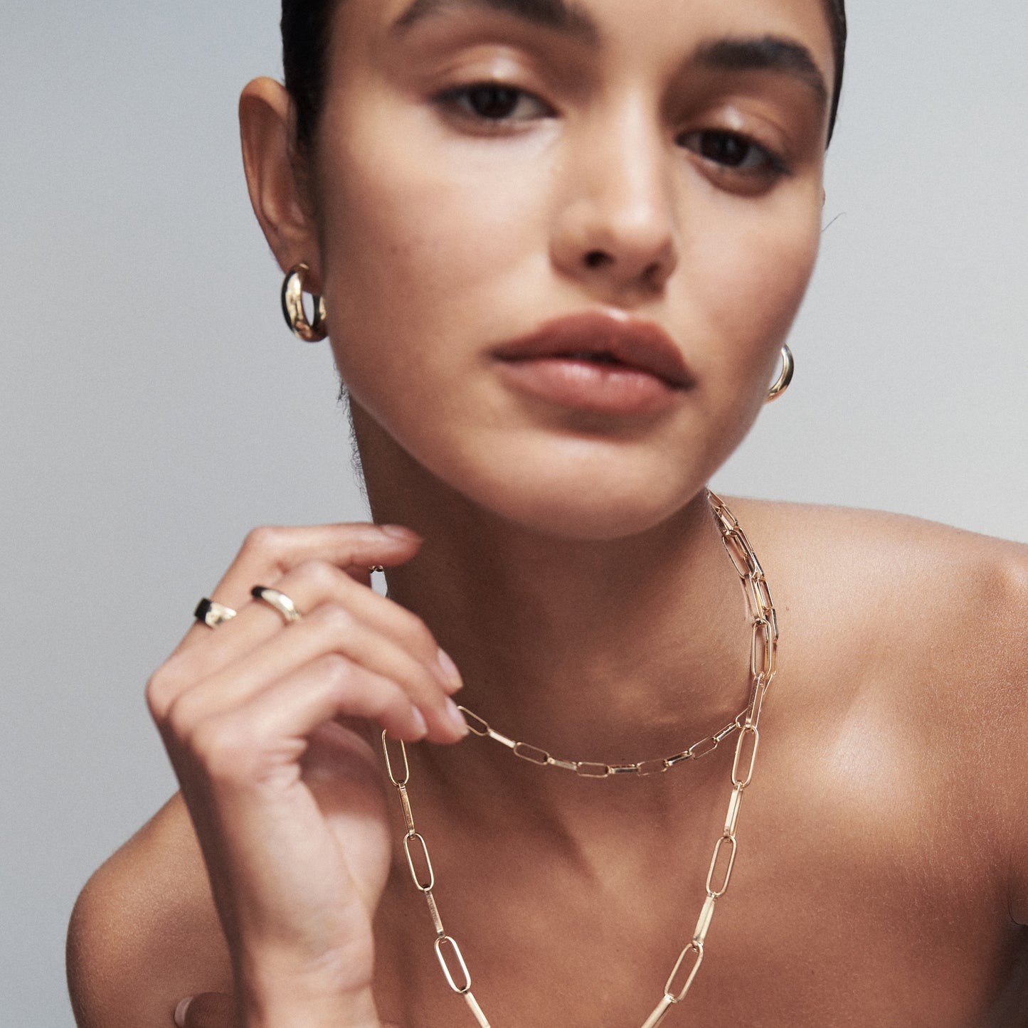 Woman wearing luxury gold jewellery: hoop earrings, a chain necklace, and rings. Elegant style, minimalist design, high-end fashion accessory.