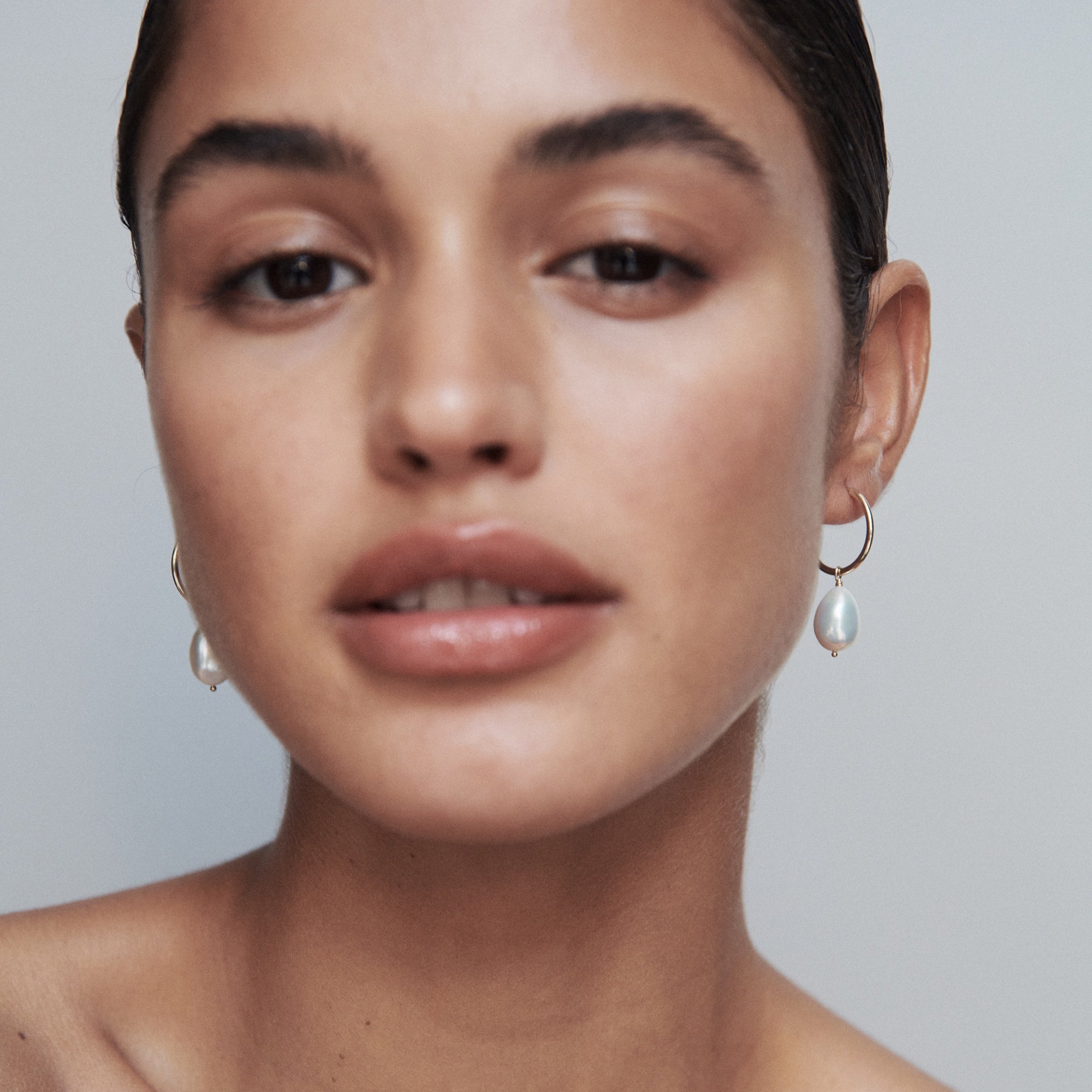 Woman wearing elegant gold hoop earrings with pearlescent drops, showcasing luxury jewellery. Minimalistic styling and serene expression.