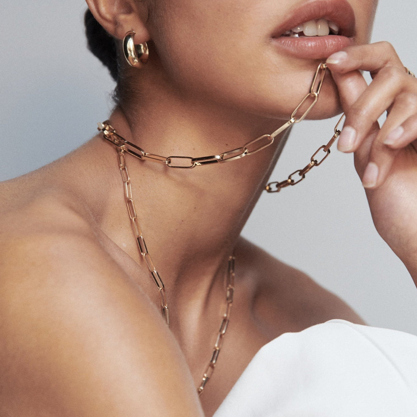 Woman wearing elegant gold chain necklace and hoop earrings, styled with a strapless white top. Luxe jewellery fashion showcasing minimalist elegance.