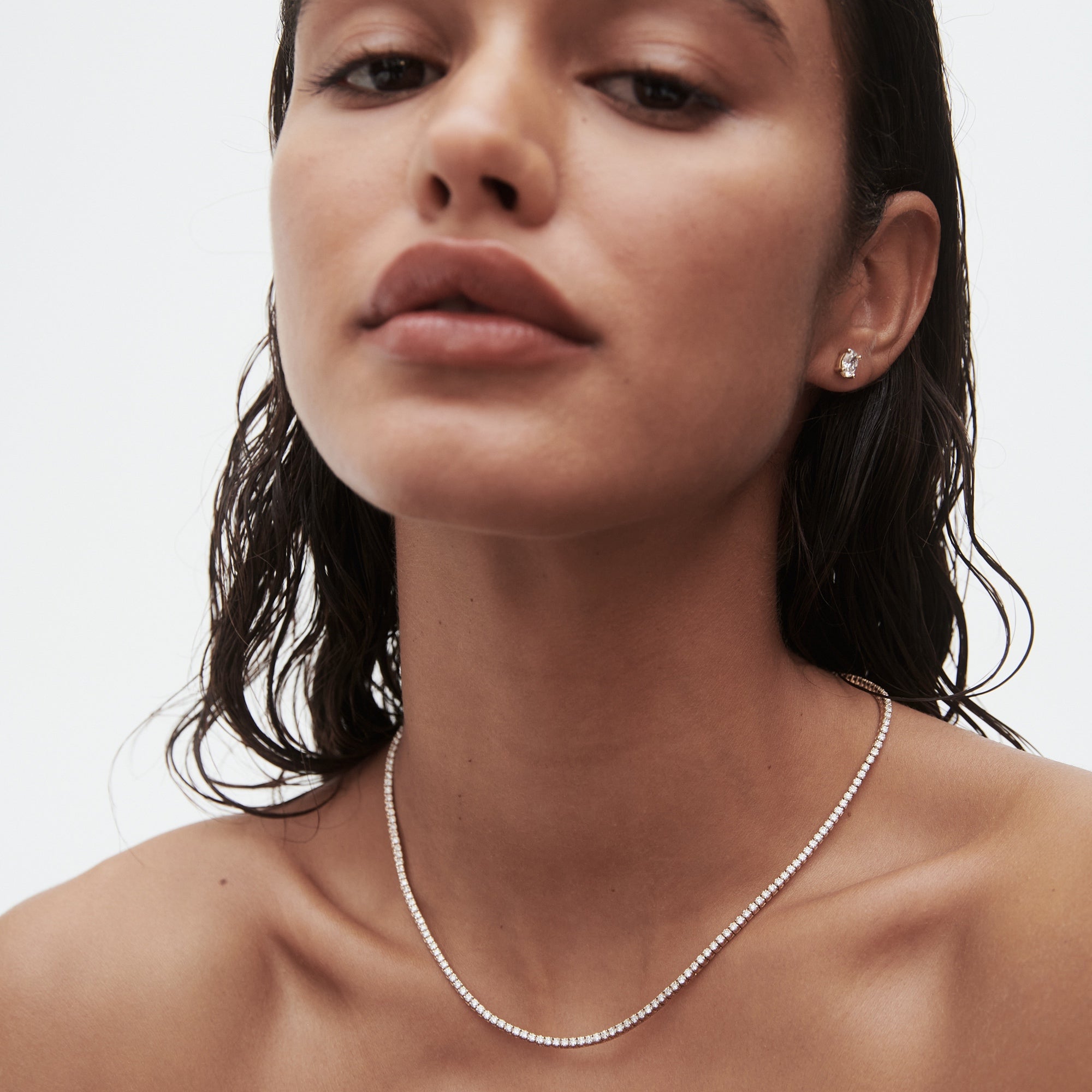 Woman wearing elegant diamond necklace and earrings, showcasing luxury jewellery. Wet hair, minimalistic style, neutral backdrop.