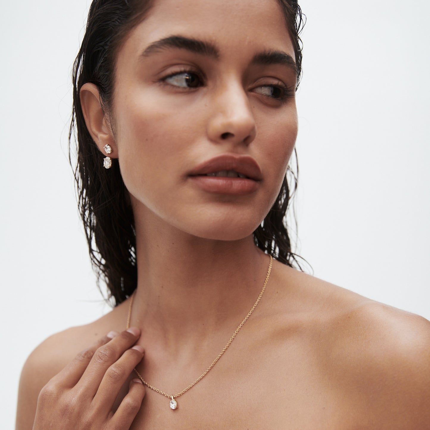Woman with wet hair wearing pearl earrings and a delicate gold necklace with a pendant, looking to the side. Luxurious jewellery display.