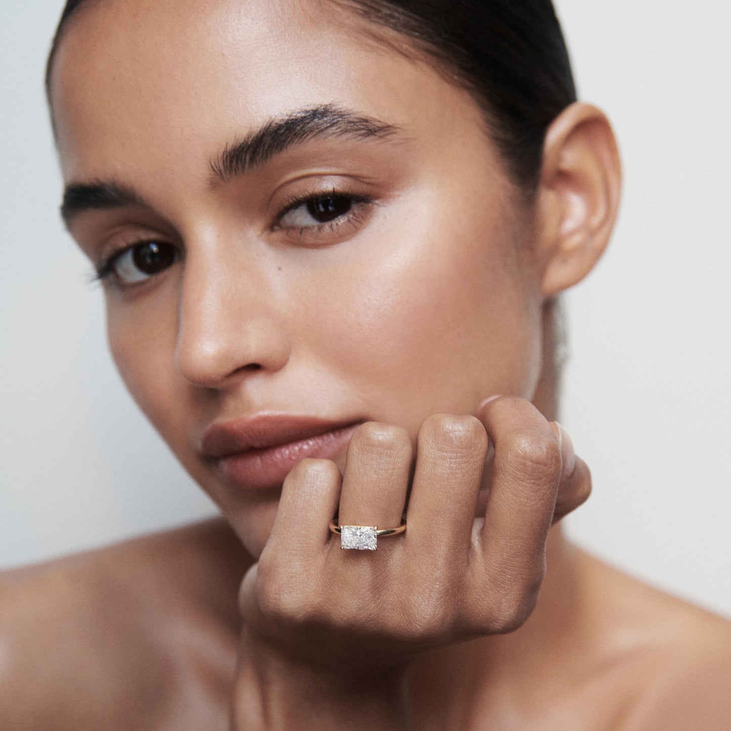 Woman displaying an elegant diamond ring on finger, showcasing luxury jewellery against a neutral background.