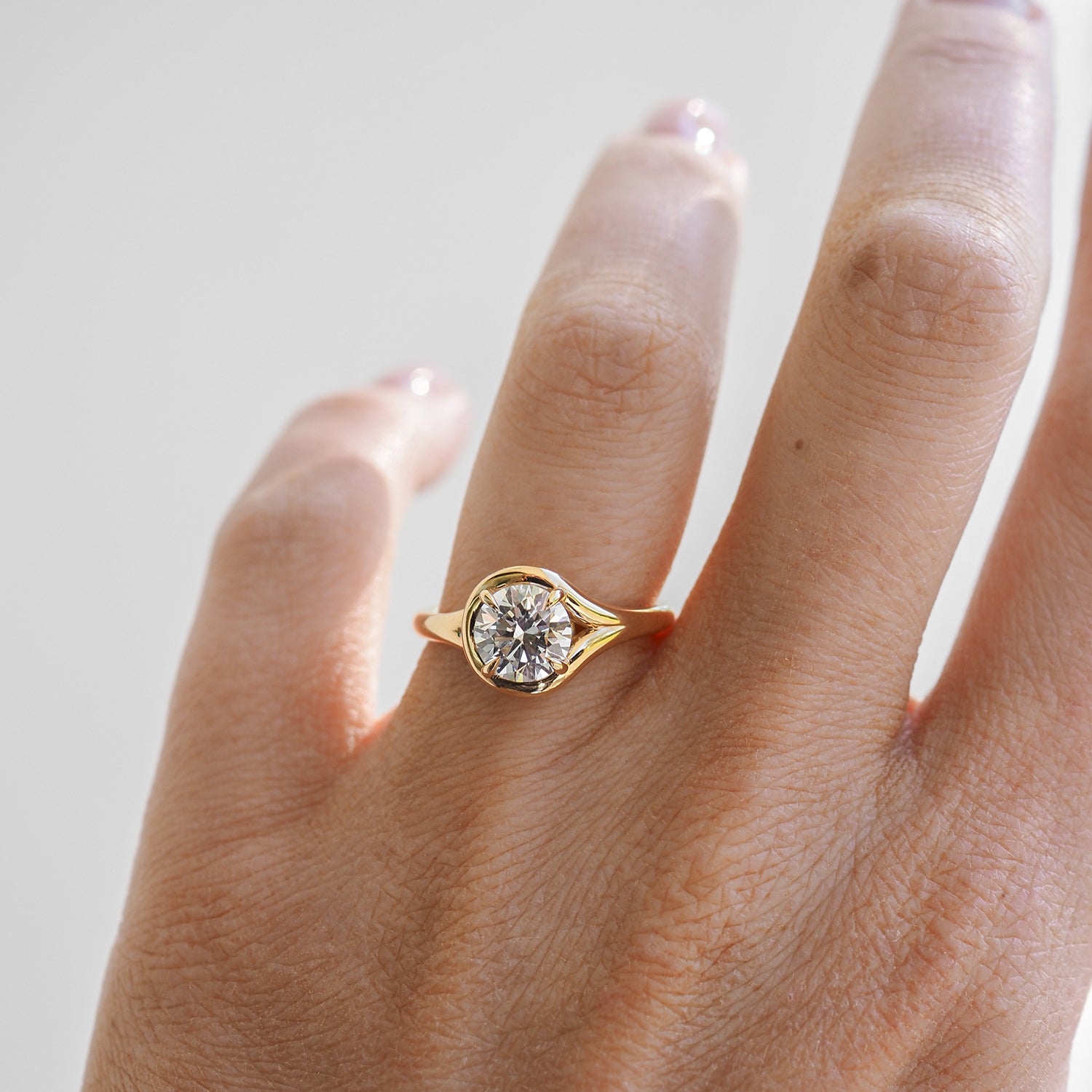 Gold band engagement ring with central round diamond on a hand. Elegant and luxurious jewellery piece under natural light.