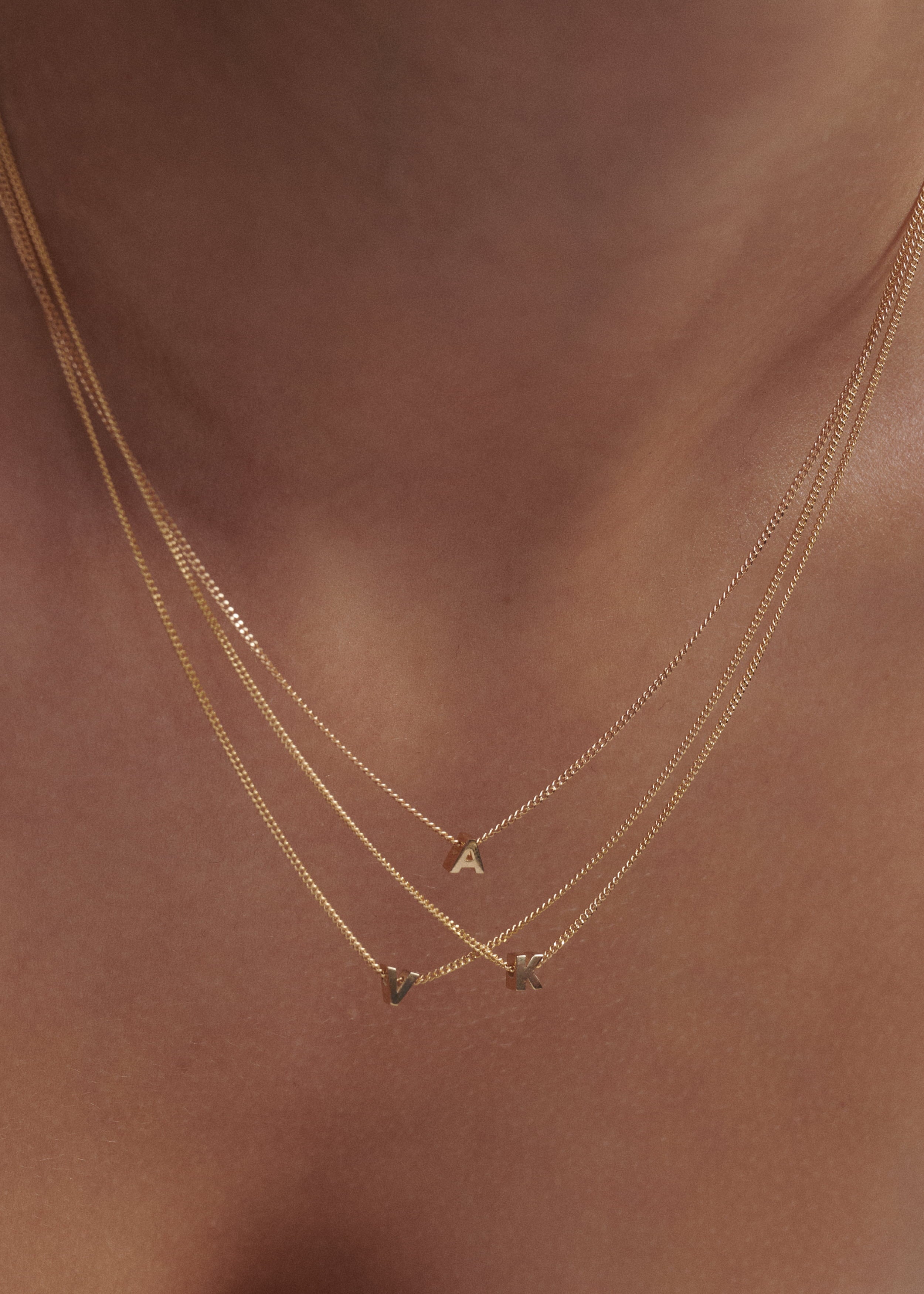Close up of woman wearing three 9ct yellow gold tiny letter necklaces 