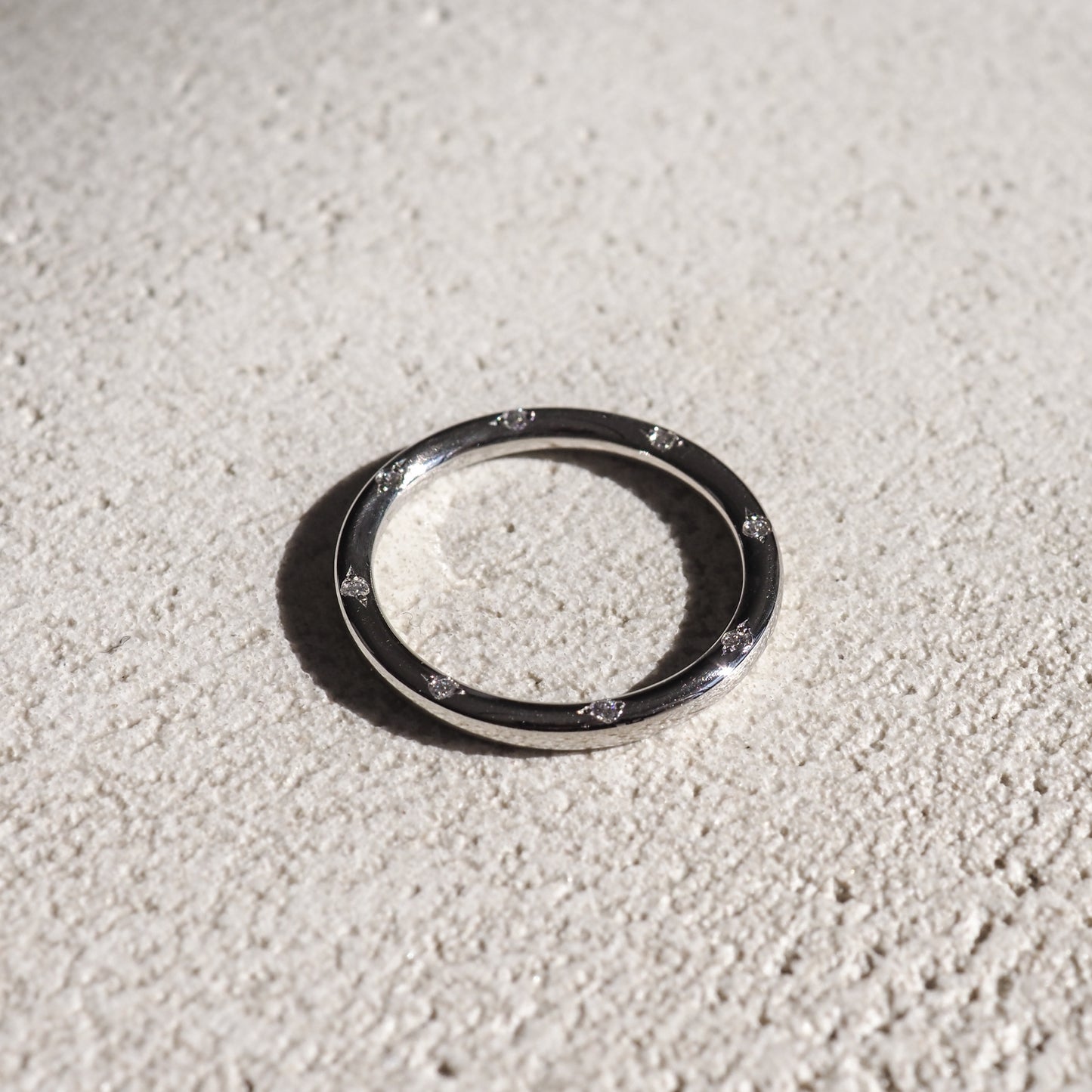 Sleek silver ring with embedded diamonds, resting on a textured light surface. High-end luxury jewellery, minimalist design.