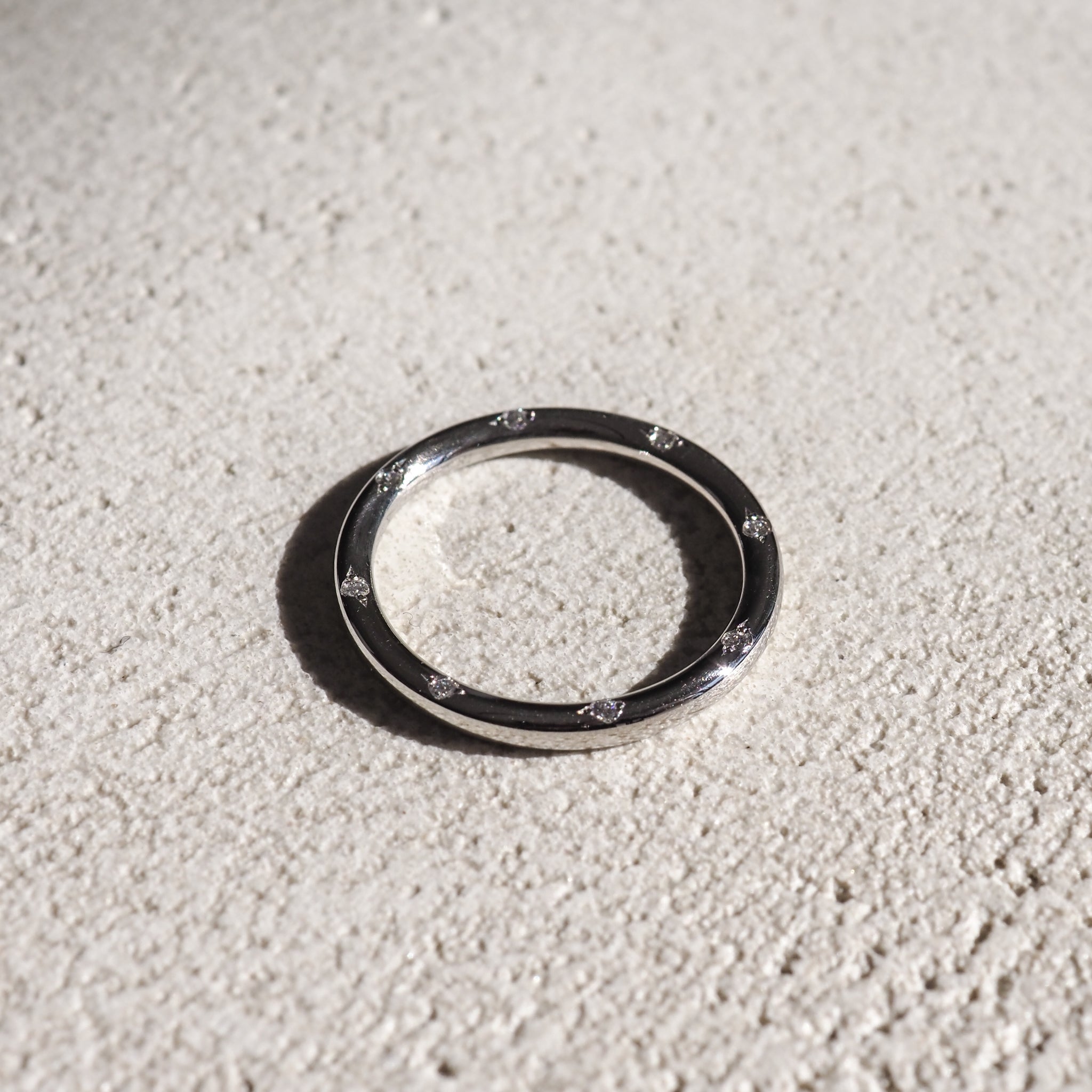 Sleek silver ring with embedded diamonds, resting on a textured light surface. High-end luxury jewellery, minimalist design.