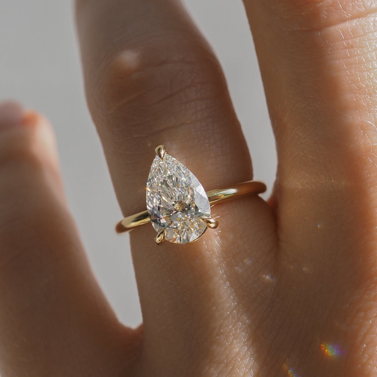 A hand wearing a luxury gold engagement ring with a large pear-shaped diamond, reflecting light.