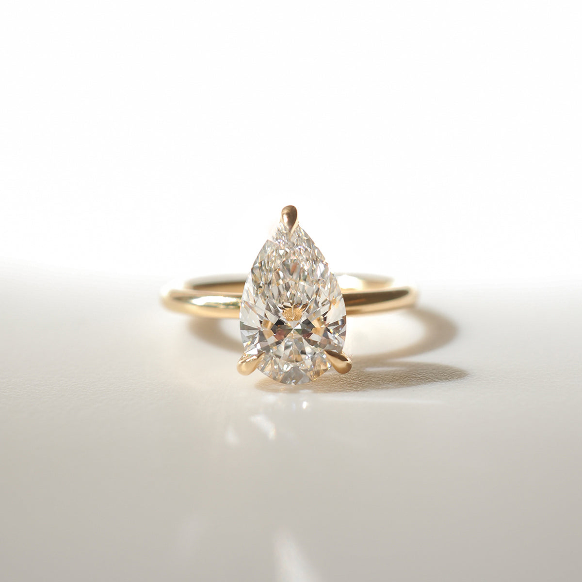 Gold ring with a pear-shaped diamond centerpiece, elegantly showcased on a light background. Perfect for luxury jewellery enthusiasts.