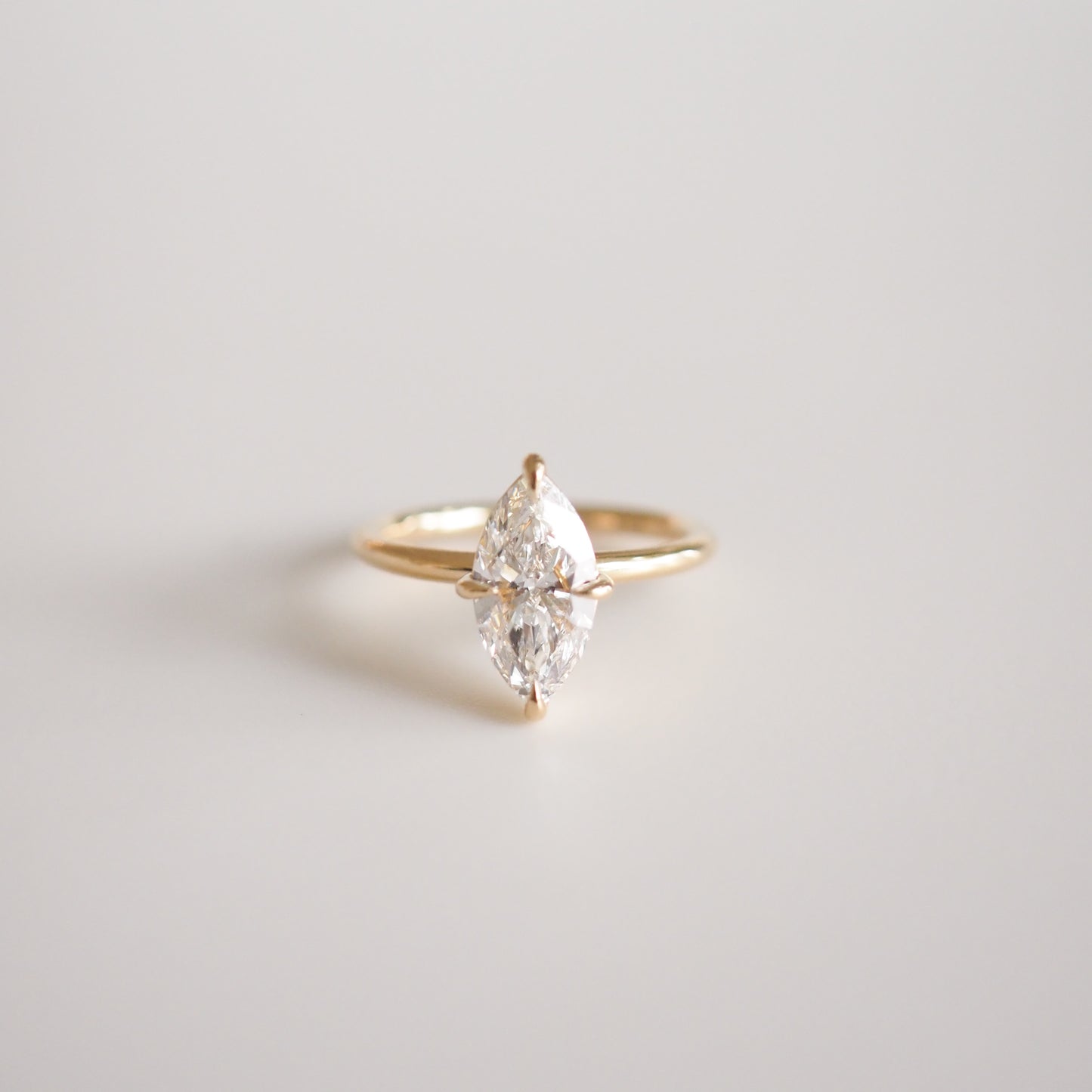 Marquise diamond ring set on a delicate gold band, resting on a soft white background. Ideal for luxury jewellery enthusiasts.