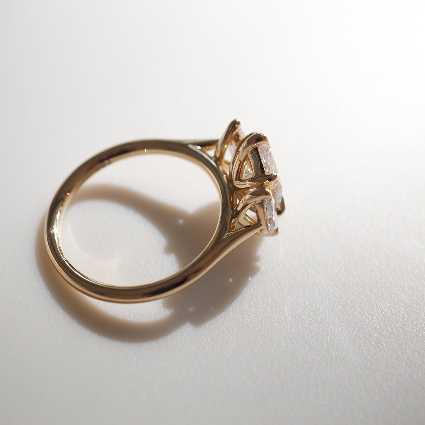 Gold ring with a trio of sparkling diamonds in a sophisticated setting, casting a shadow on a smooth surface. Perfect for luxury jewellery lovers.