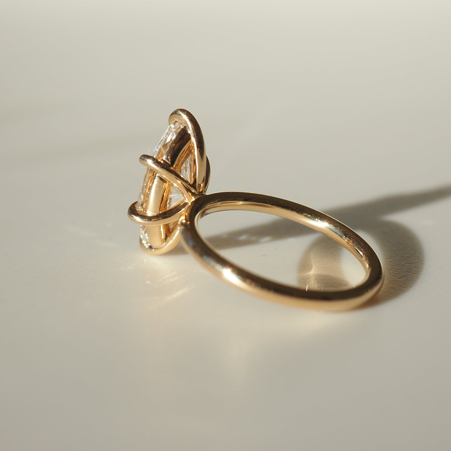 Gold ring with a large, clear marquise-cut gemstone set in a sleek, minimalist design, casting a soft shadow on a light surface.