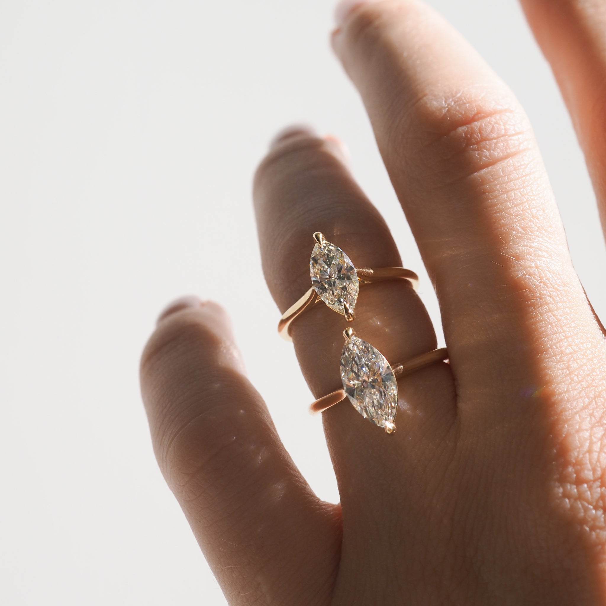 Hand wearing two gold rings with large marquise-cut diamonds, elegantly displayed under soft lighting, showcasing luxury jewellery.
