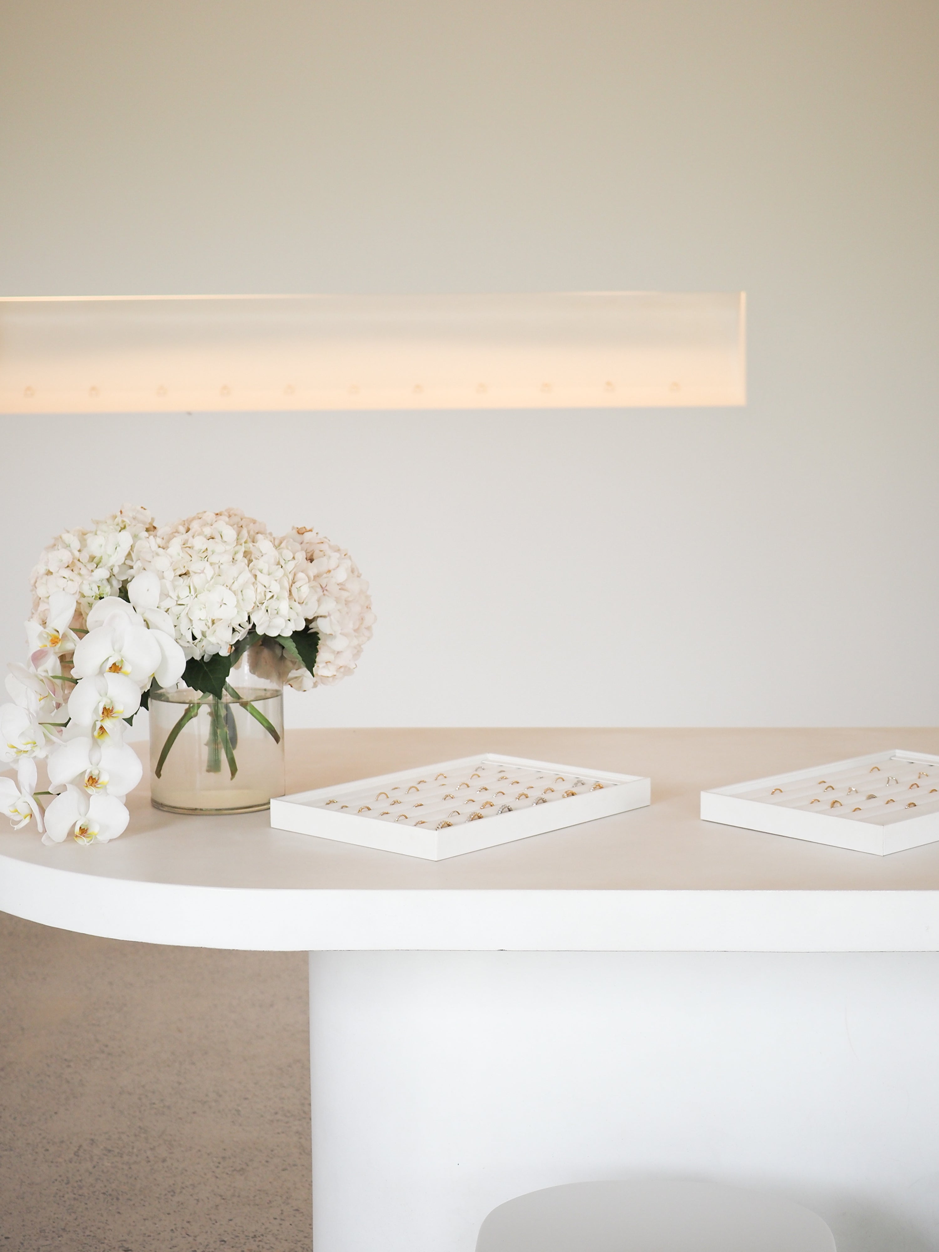 Elegant display of luxury jewellery pieces on a white table with a vase of white orchids and hydrangeas, set against a minimalist backdrop.