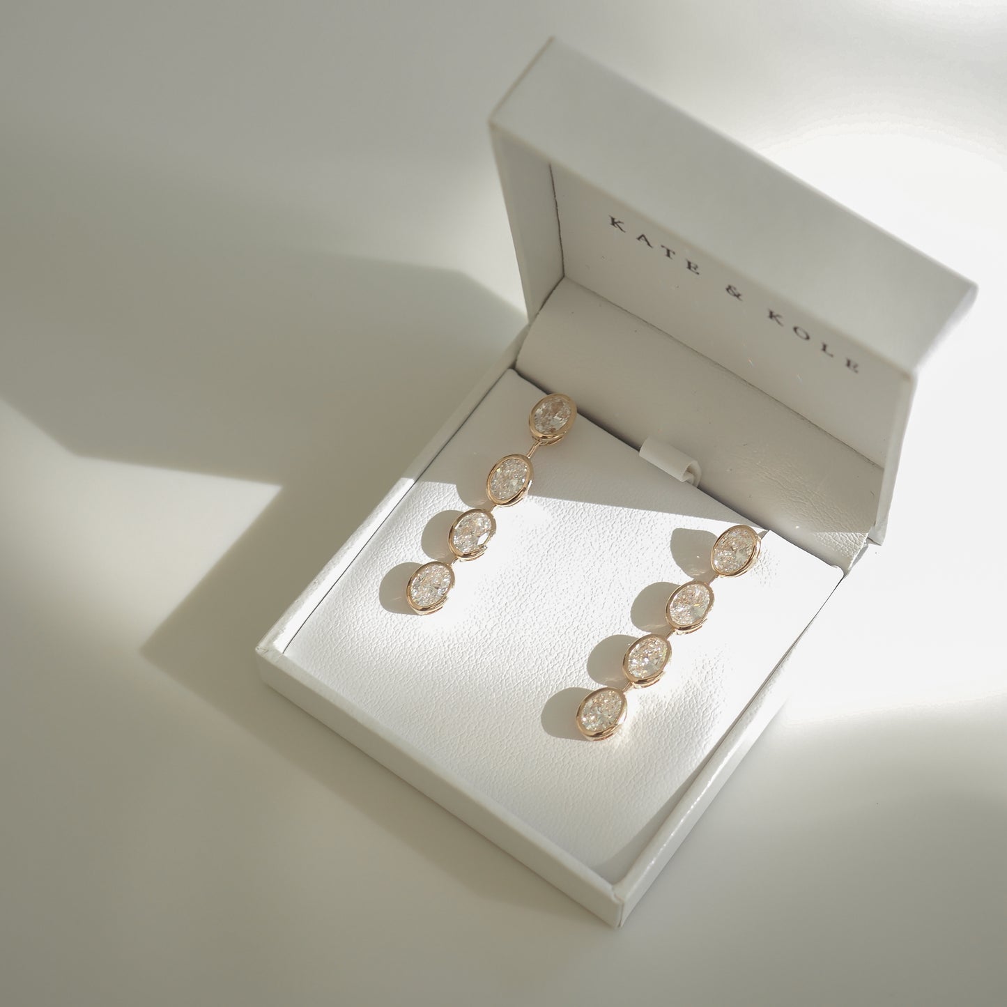 Elegant gold earrings with round gemstones displayed in a white jewellery box, casting soft shadows, exemplifying luxury fashion.