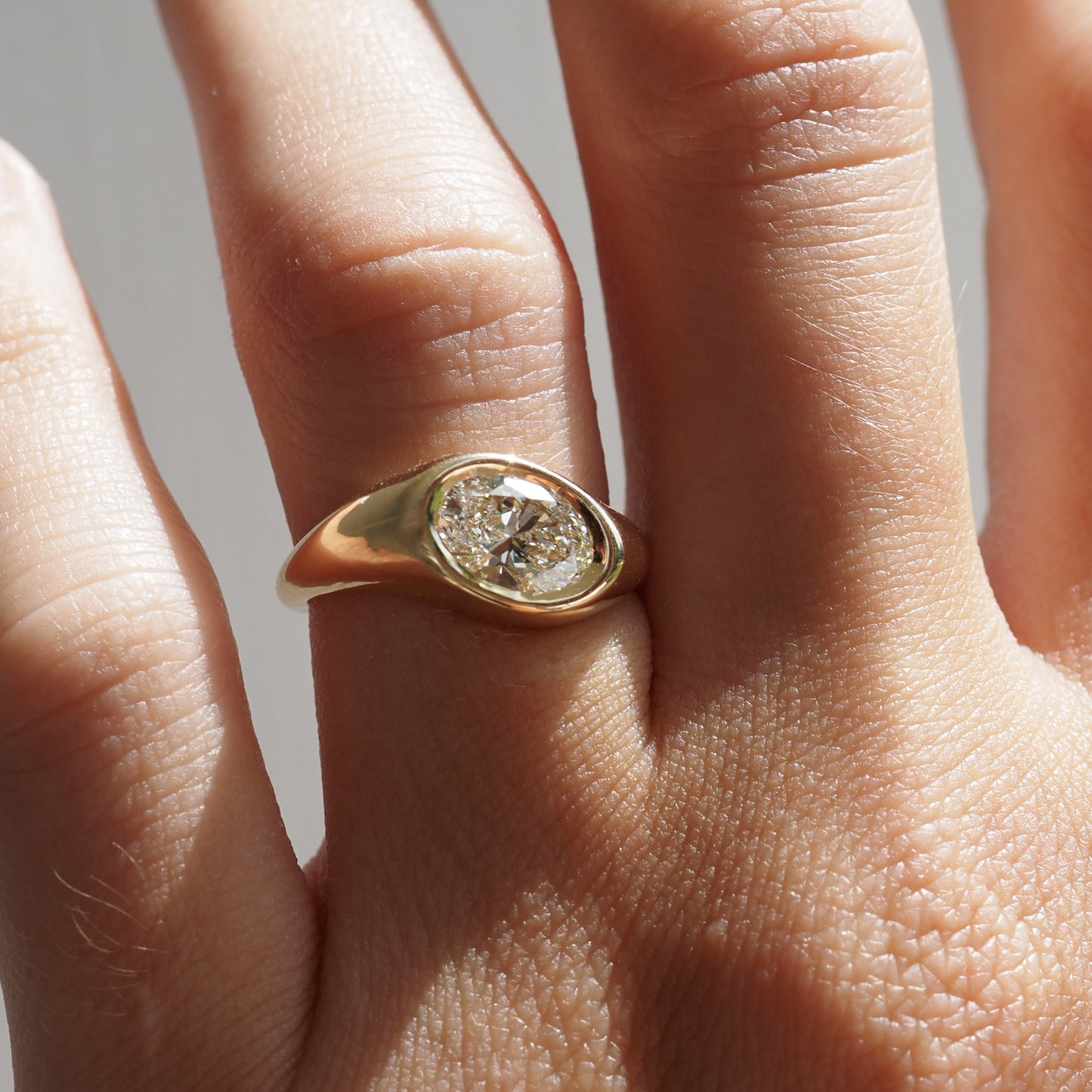 Gold ring with a diamond on a person's finger against a neutral background