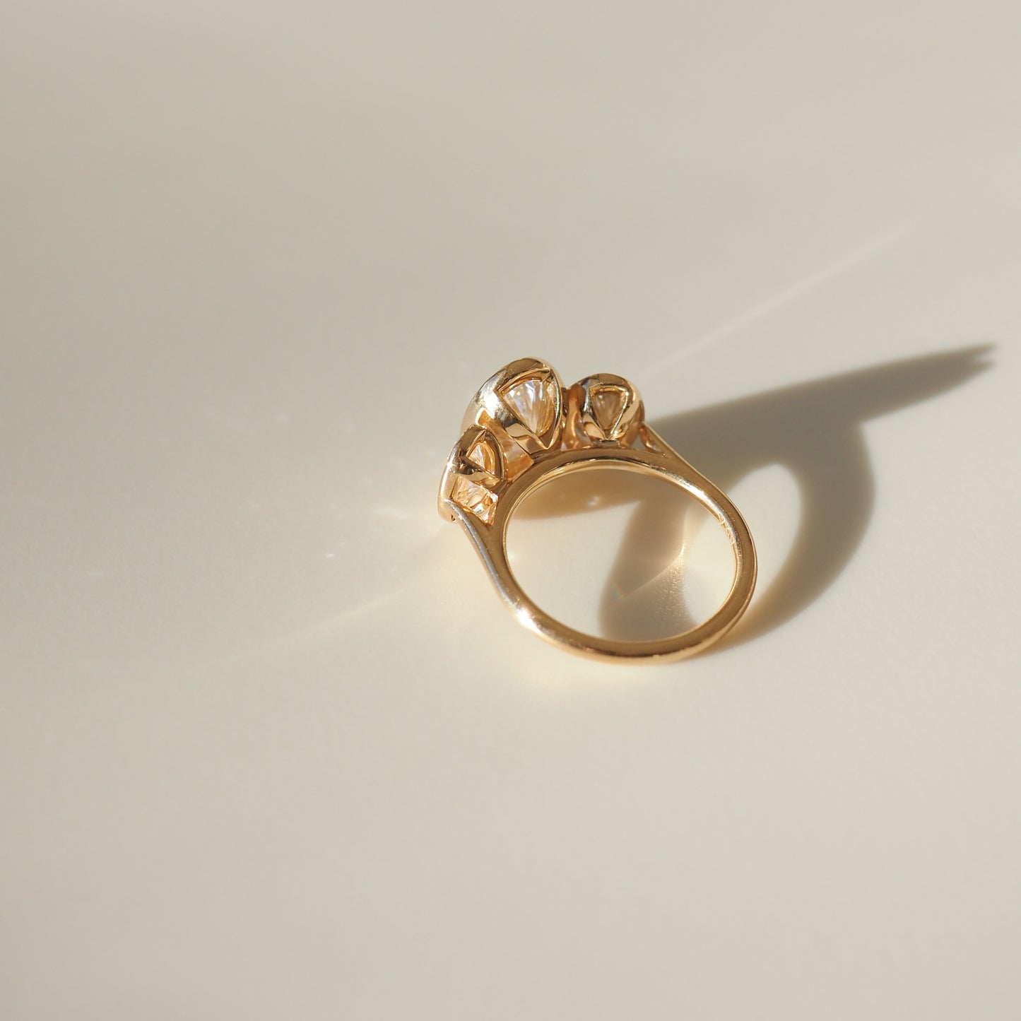 Elegant gold ring featuring three sparkling gemstones, casting a soft shadow on a light surface, exemplifying luxury craftsmanship.