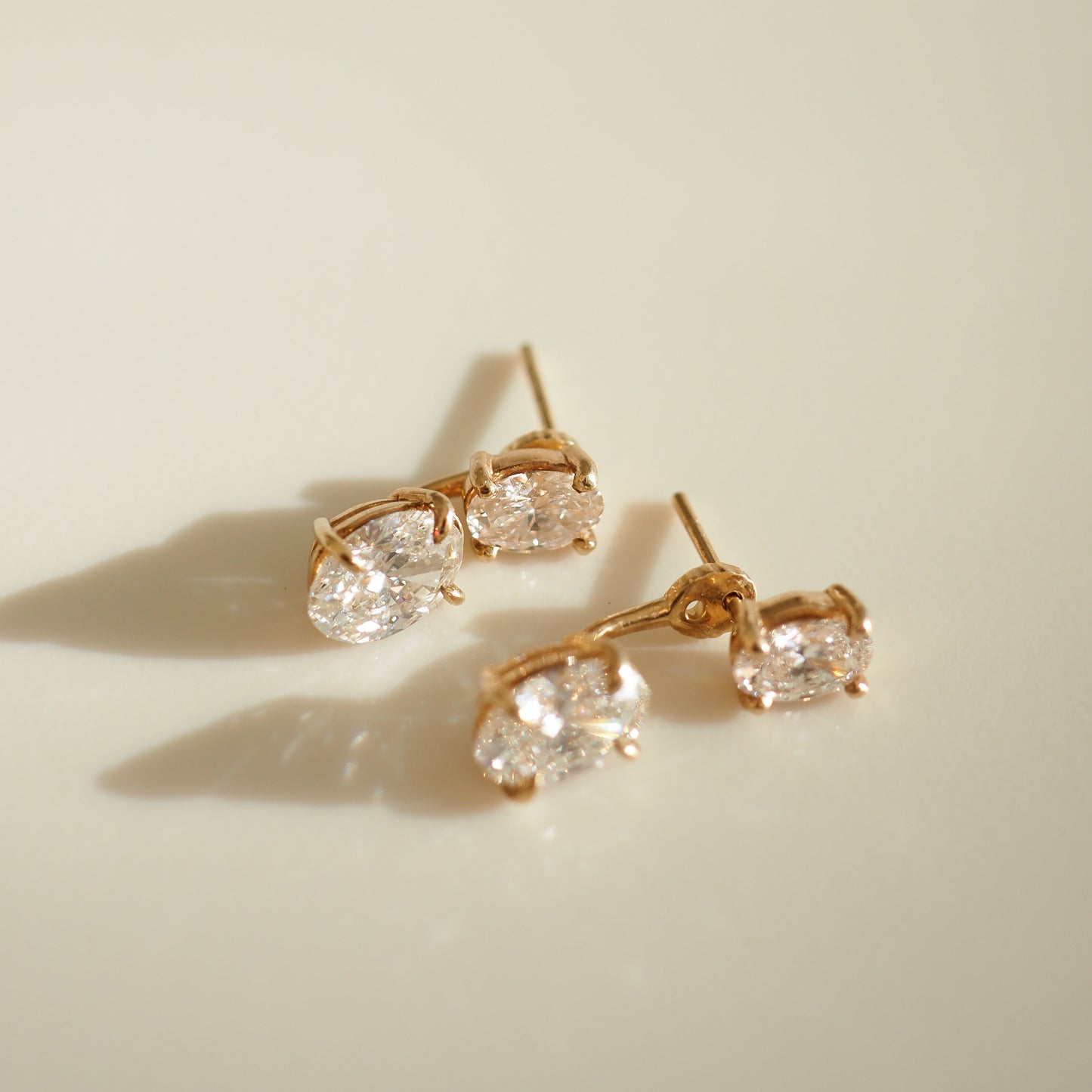 Gold stud earrings with sparkling oval diamonds on a soft, light background. Elegantly captures luxury jewellery design and craftsmanship.