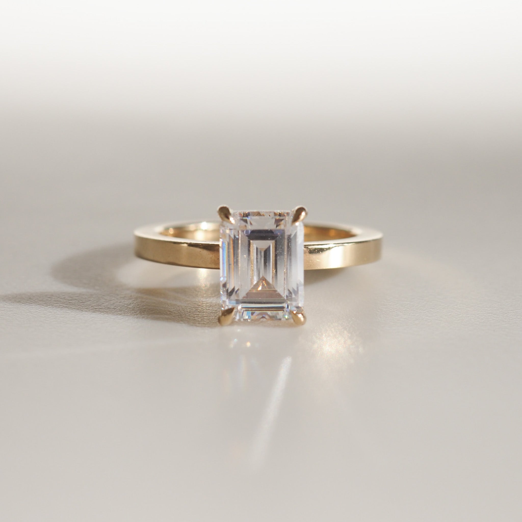 Emerald-cut diamond ring set in a simple gold band, elegantly displayed on a soft, neutral background.