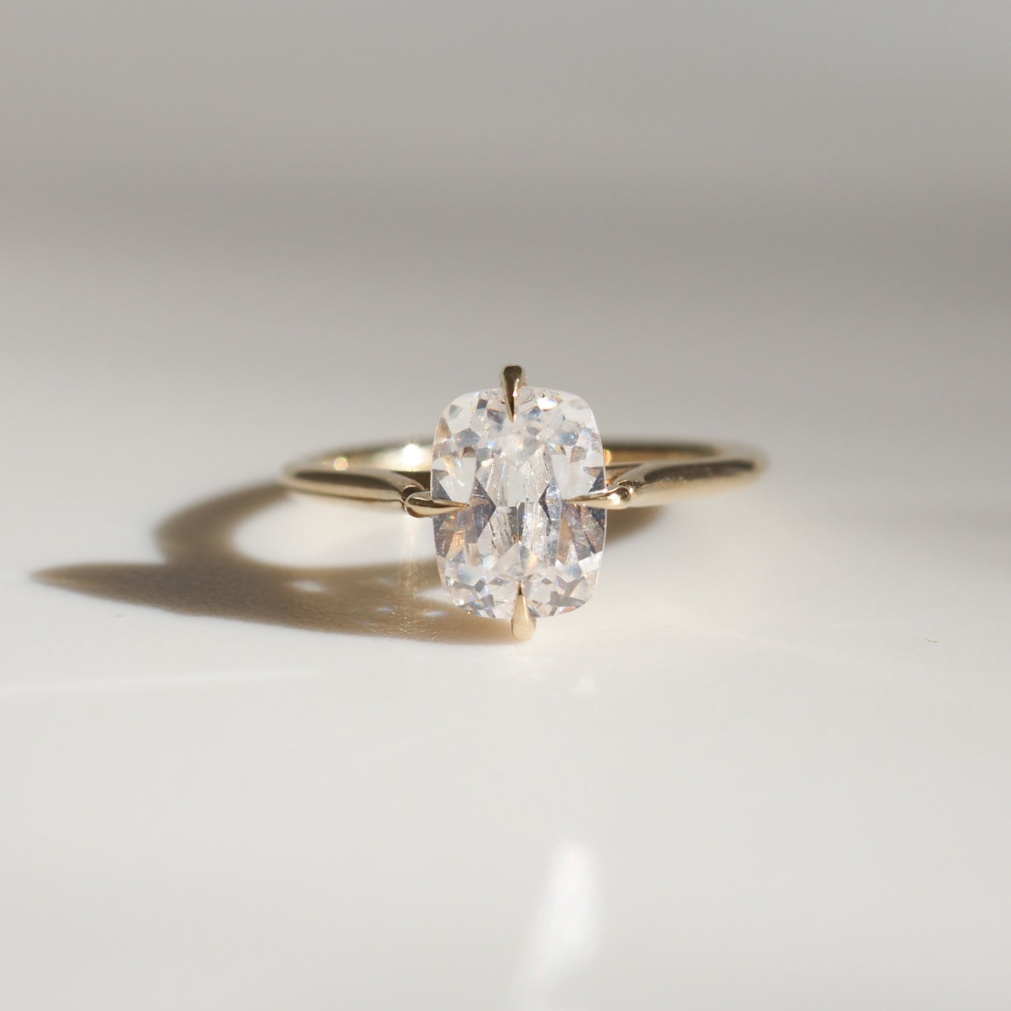 Elegant solitaire diamond ring with a gold band on a reflective surface, casting a delicate shadow. Perfect for luxury jewellery lovers.