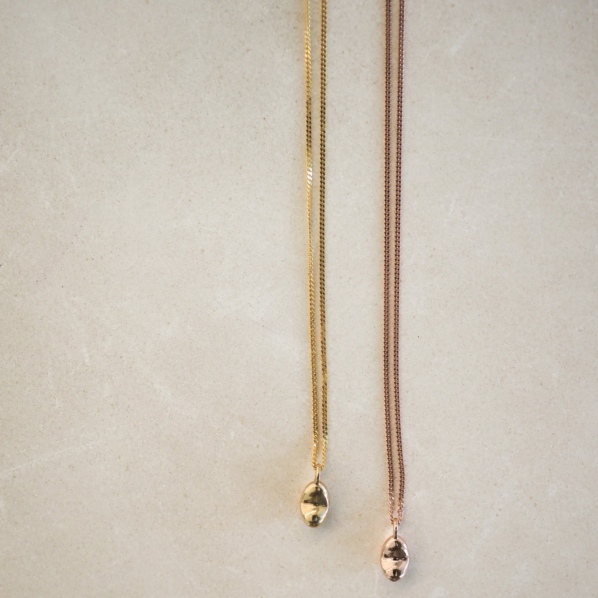 Two elegant necklaces on a light surface; one gold with a gold pendant, the other rose gold with a matching pendant. Luxury jewellery display.