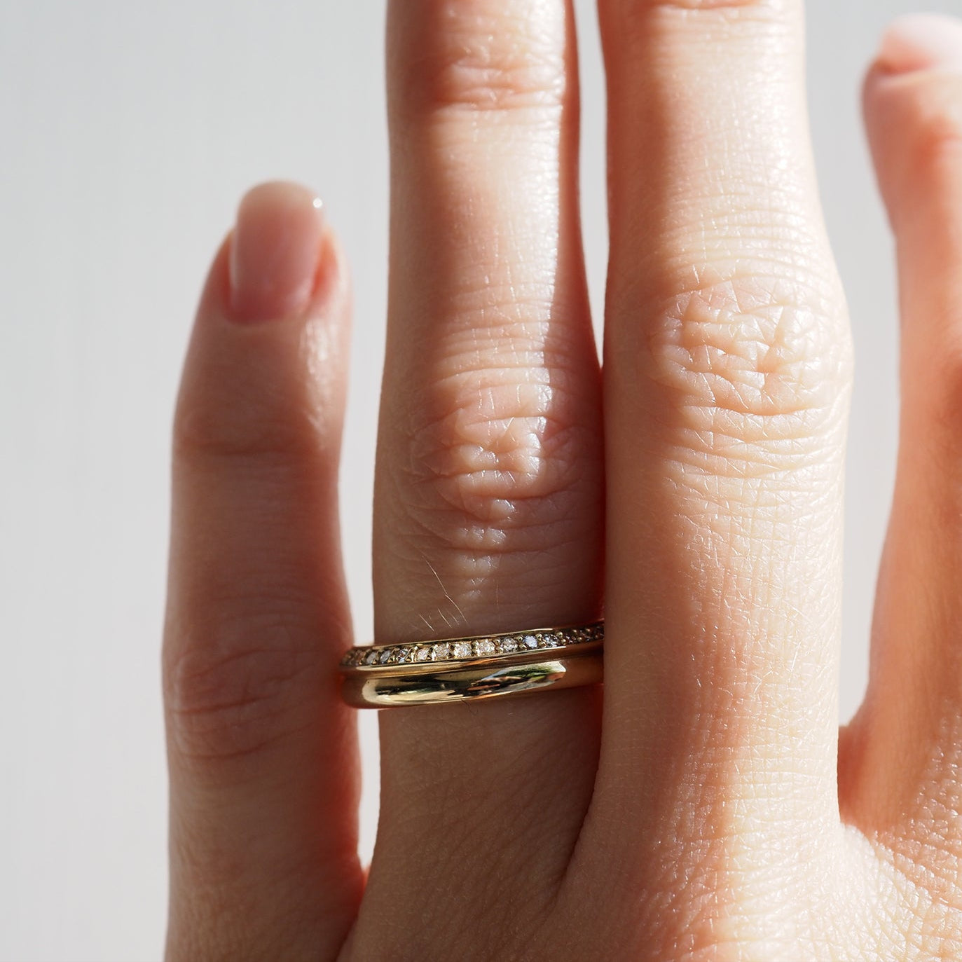 Close-up of a hand wearing a gold ring with embedded diamonds on the ring finger, showcasing luxury jewellery design under soft lighting.