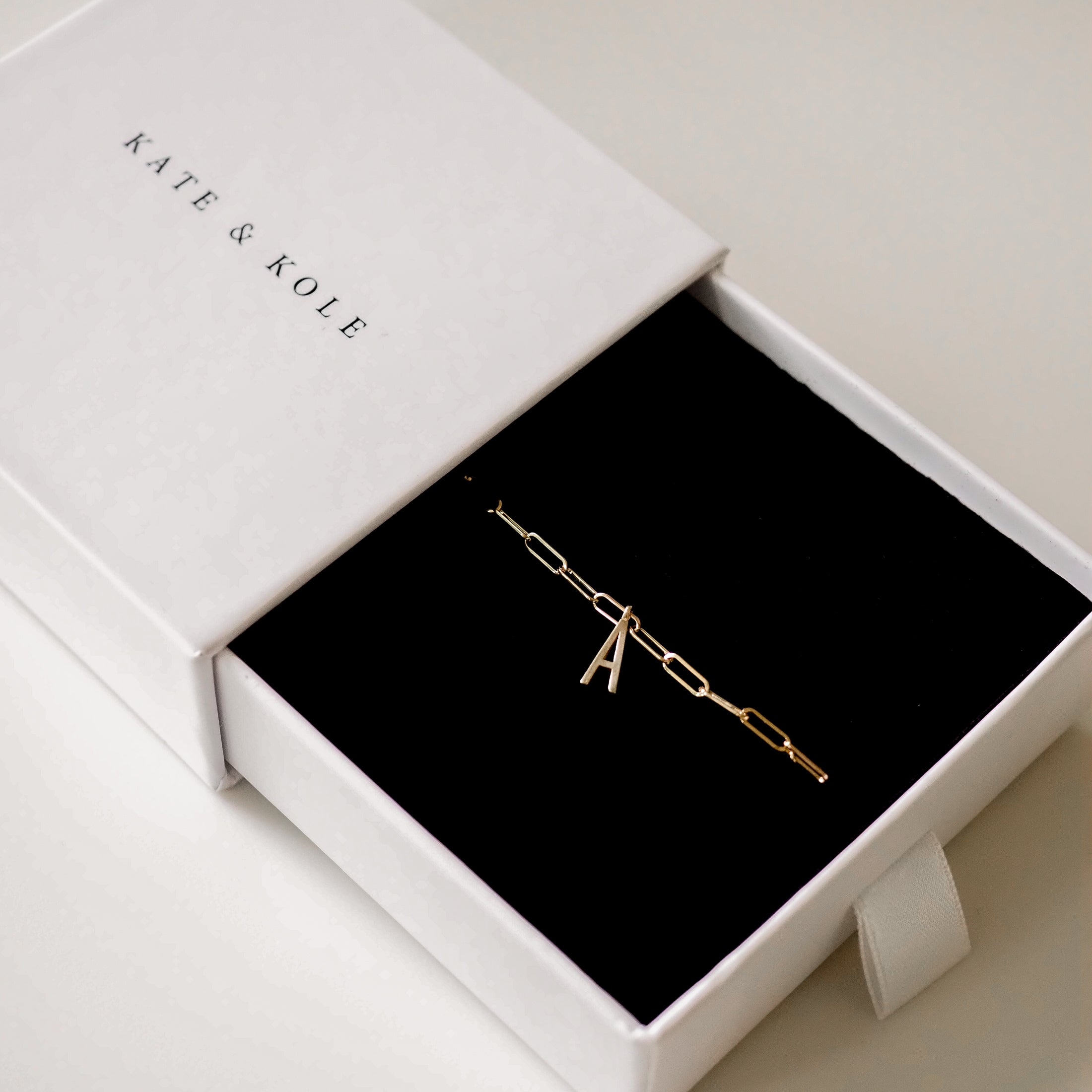 Gold chain bracelet with an 'A' charm, presented in an elegant Kate & Kole branded white box with a black interior.