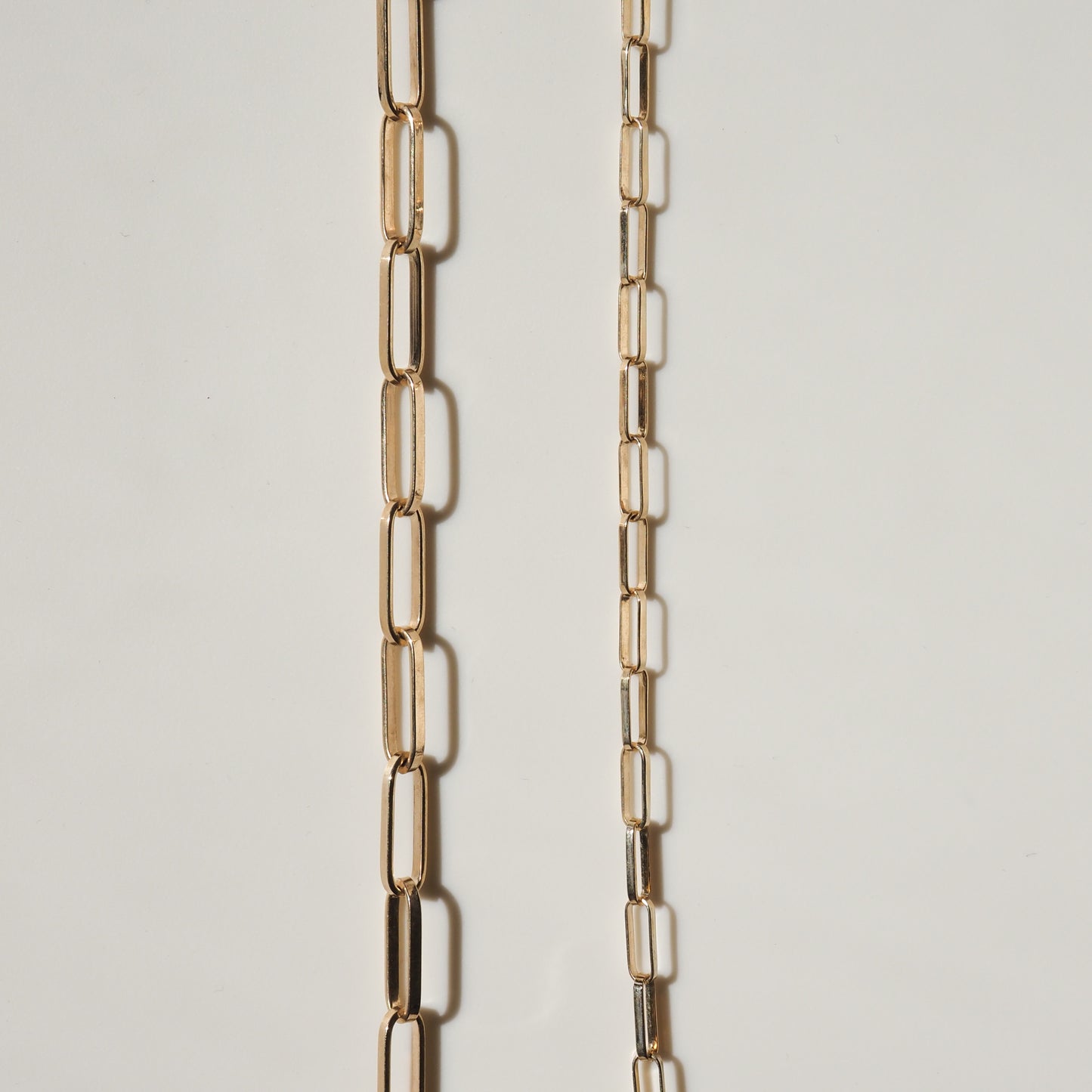 Two elegant gold chain necklaces with elongated rectangular links on a light background, showcasing luxury and high-end jewellery design.