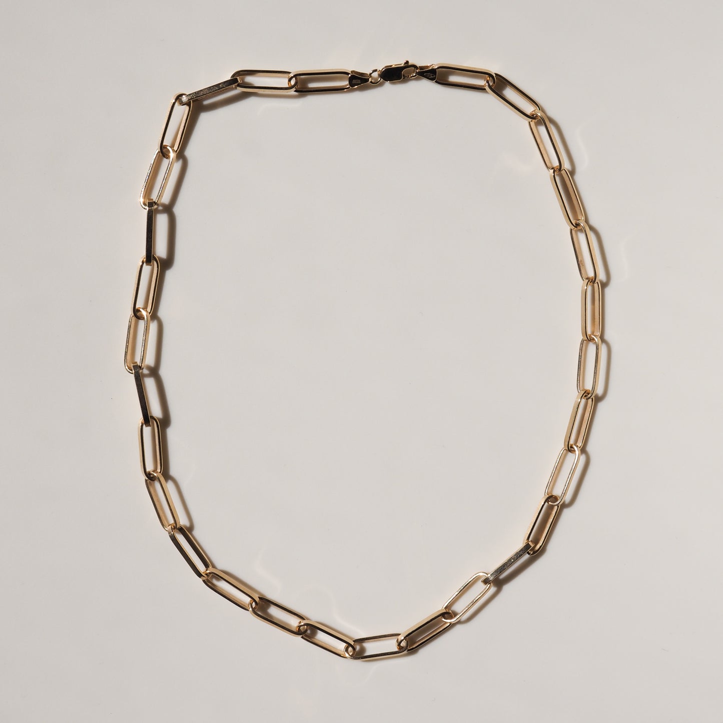 Gold chain necklace with elongated links on a white background, showcasing minimalistic luxury jewellery design.