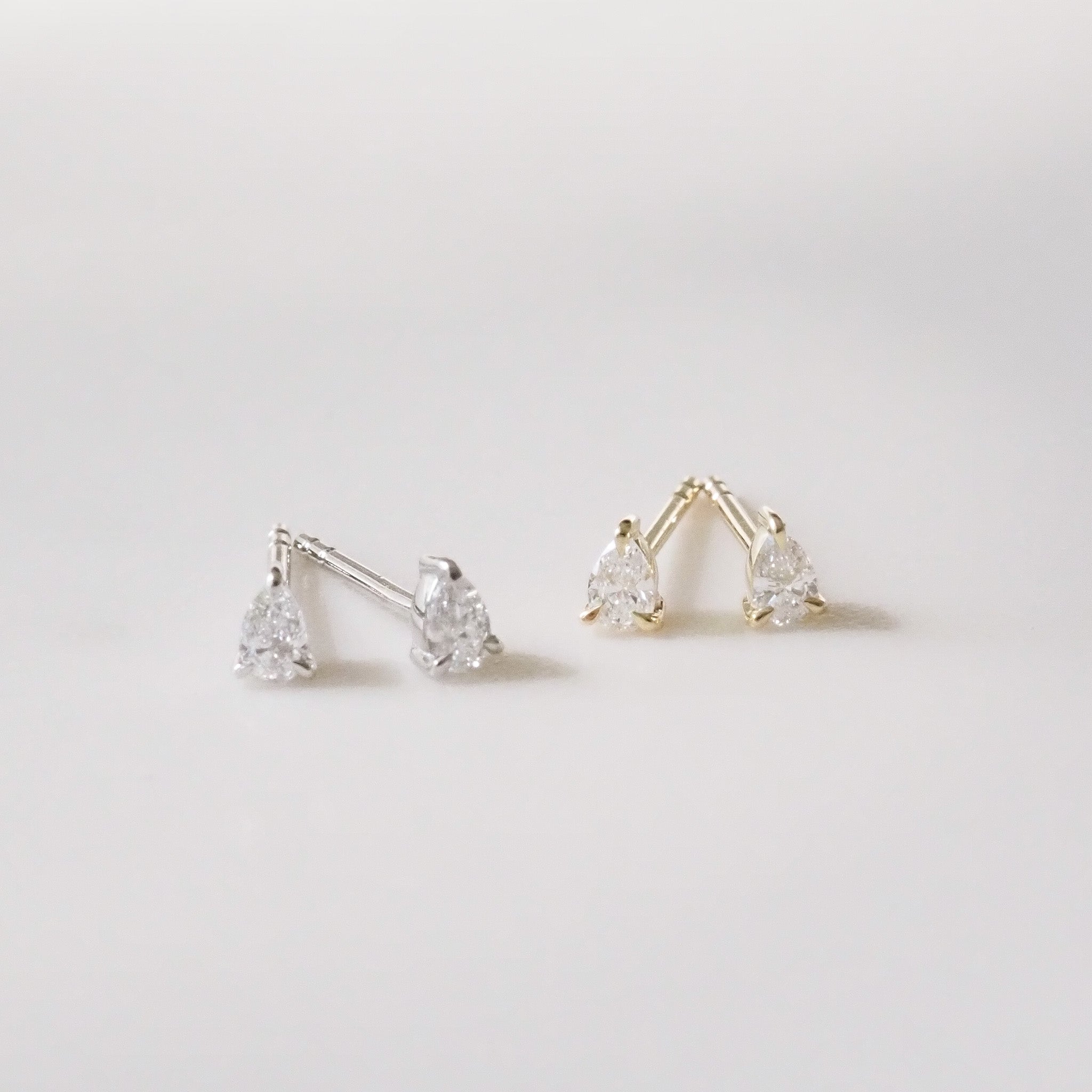 Pair of gold and silver pear-shaped earrings on a light gray background