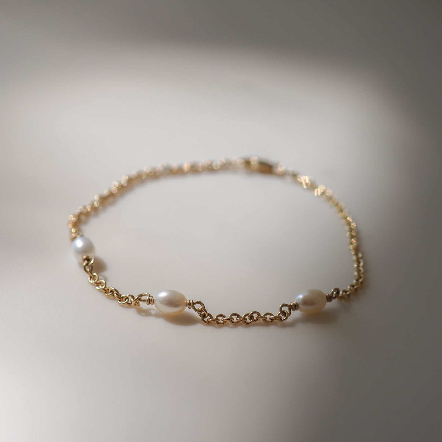 Elegant gold bracelet adorned with four pearls, delicately linked by a fine chain, set against a softly lit background.