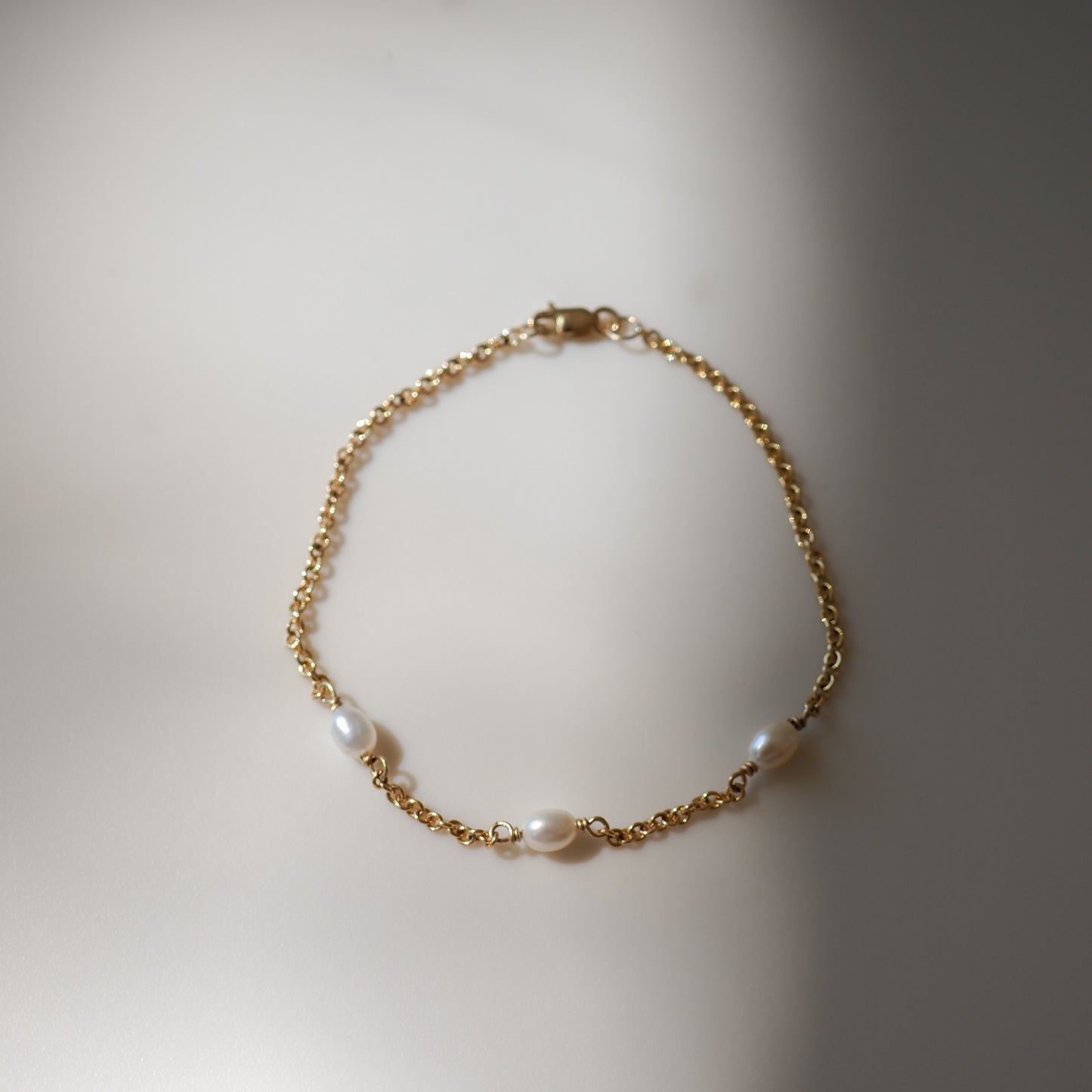 Elegant gold chain bracelet with three freshwater pearls, beautifully laid out on a soft, light surface.