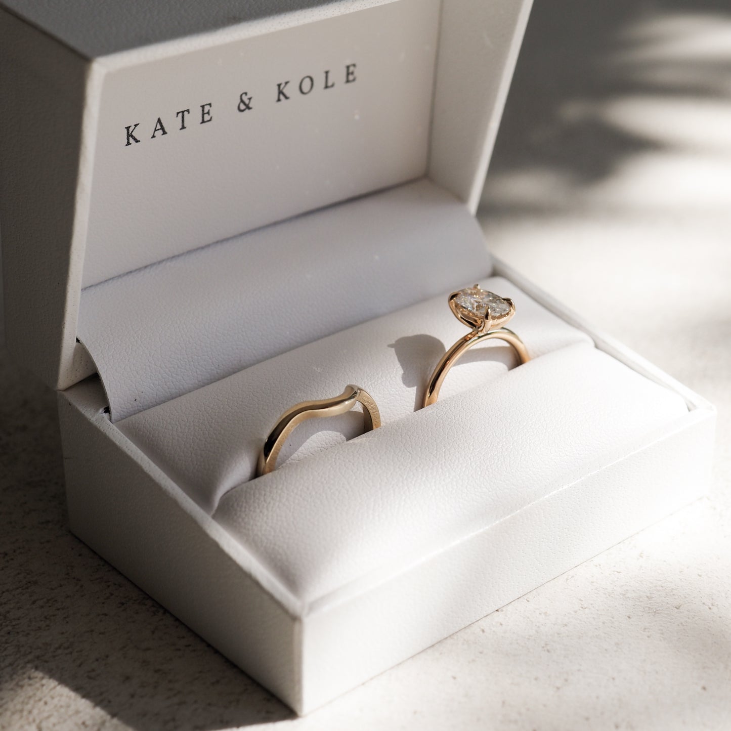 Elegant gold ring set with diamond in a white Kate & Kole jewellery box, bathed in soft light.