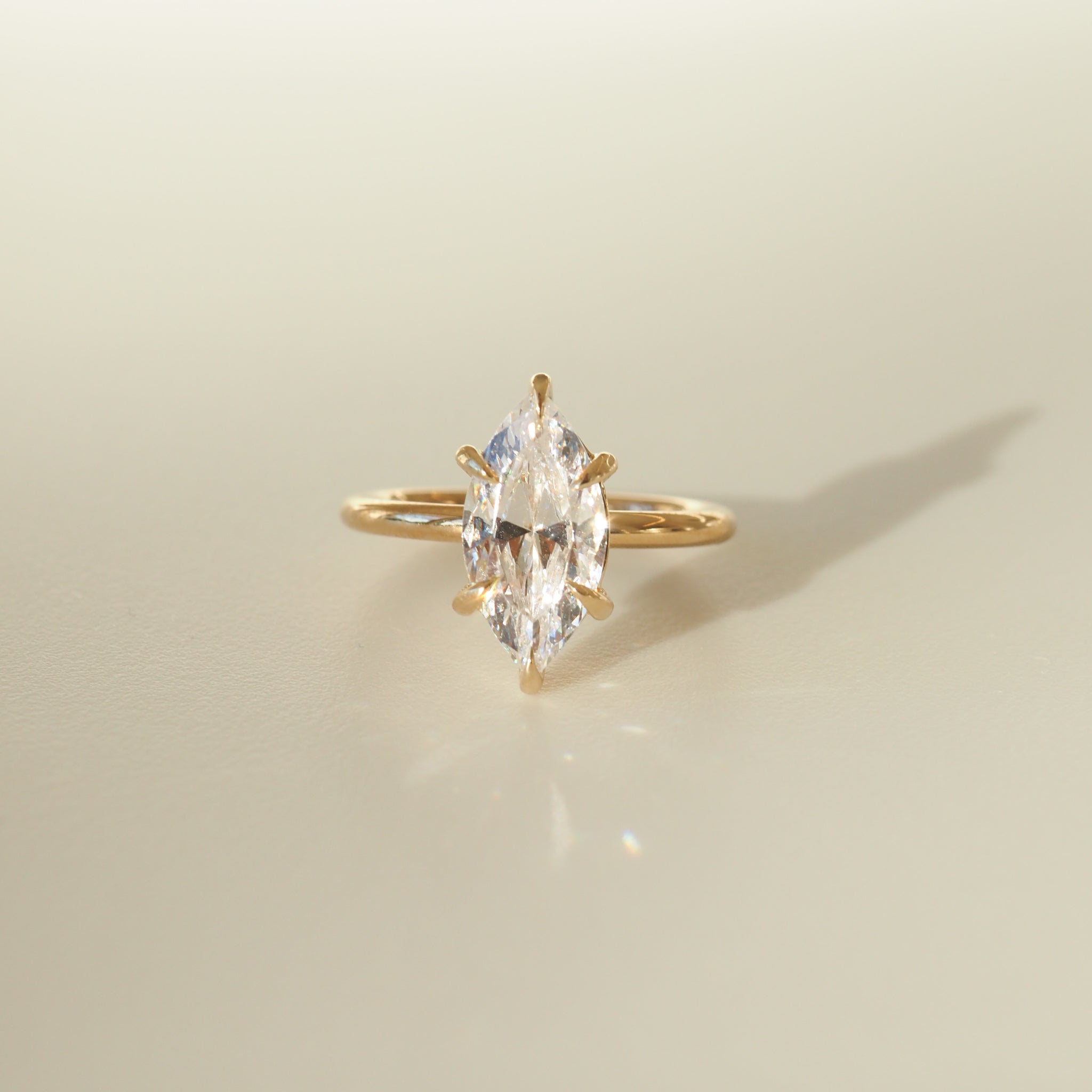 Marquise-cut diamond ring set on a sleek gold band, casting a soft shadow on a neutral background. Ideal for luxury jewellery enthusiasts.