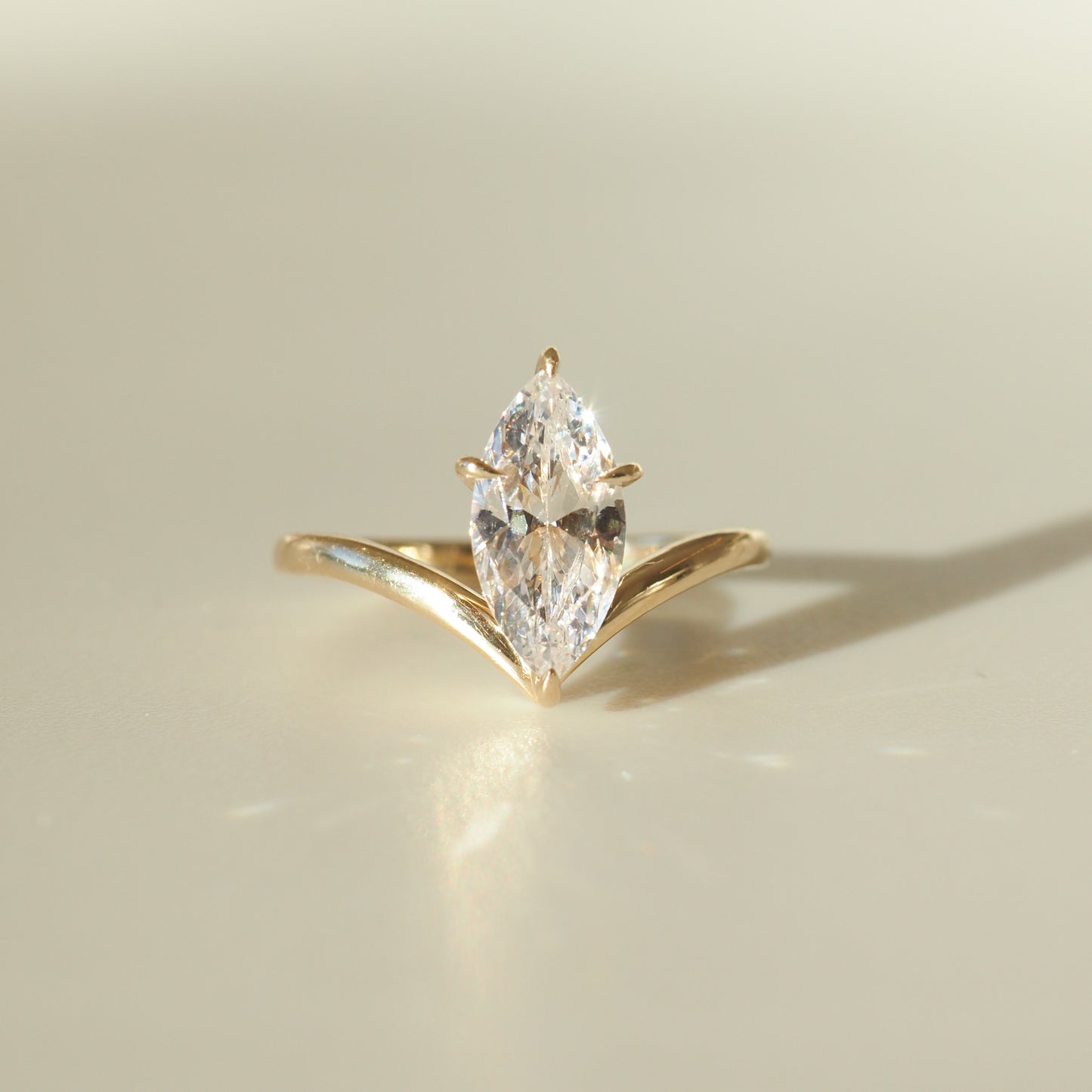 Marquise-cut diamond solitaire ring in a gold band setting, reflecting light on a neutral background. Elegant, luxury jewellery piece.