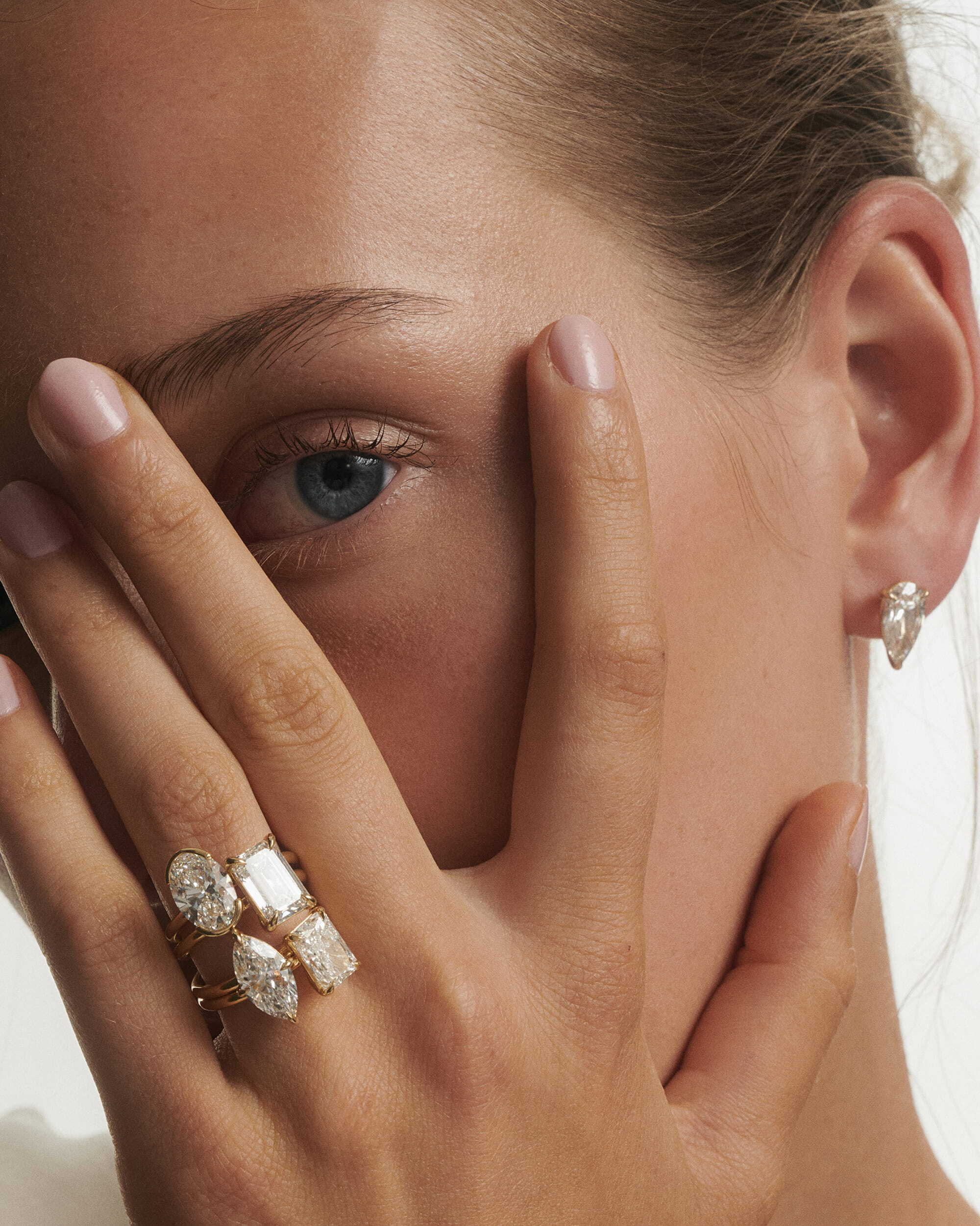 Close-up of a hand on a woman's face with diamond rings, covering one eye.