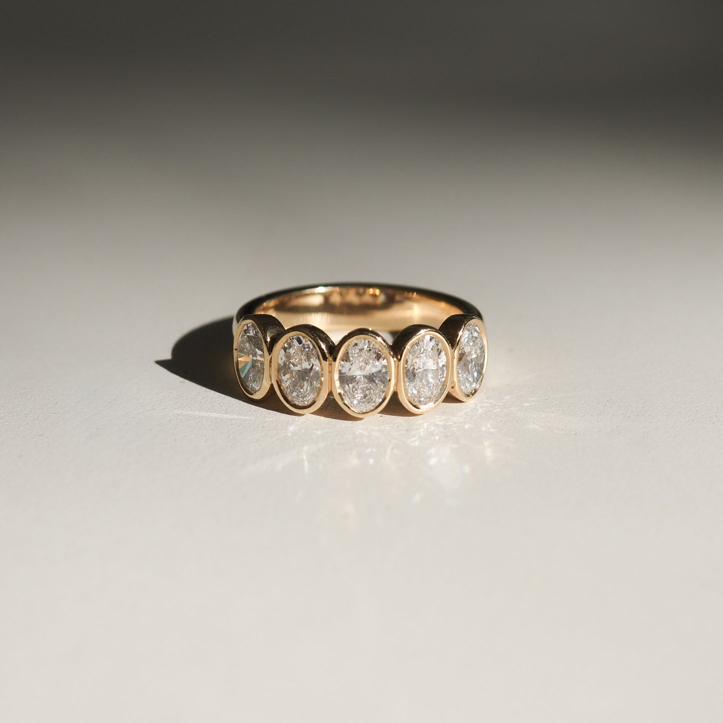 Gold ring with five oval diamond settings, displayed on a reflective surface. Elegant and luxurious jewellery design.
