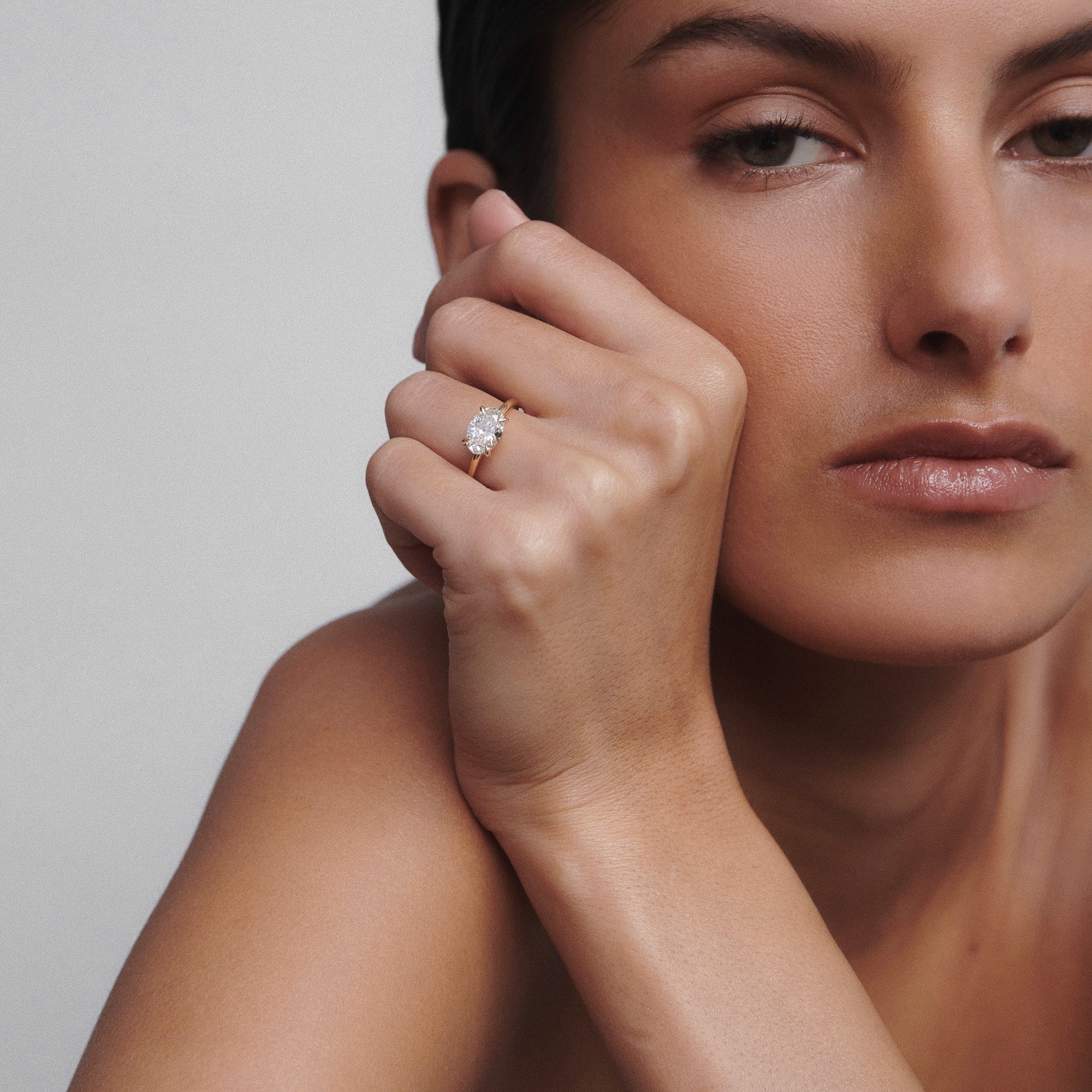 Woman with sleek hair wearing an elegant diamond ring, displayed on her finger, in a luxurious and minimalist setting.