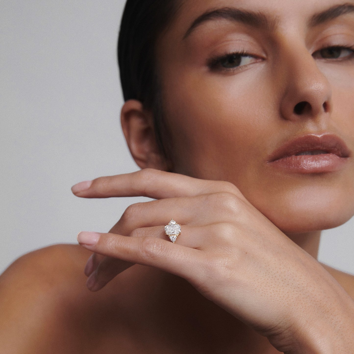Woman showcasing a luxury diamond engagement ring on her finger, against a neutral background.