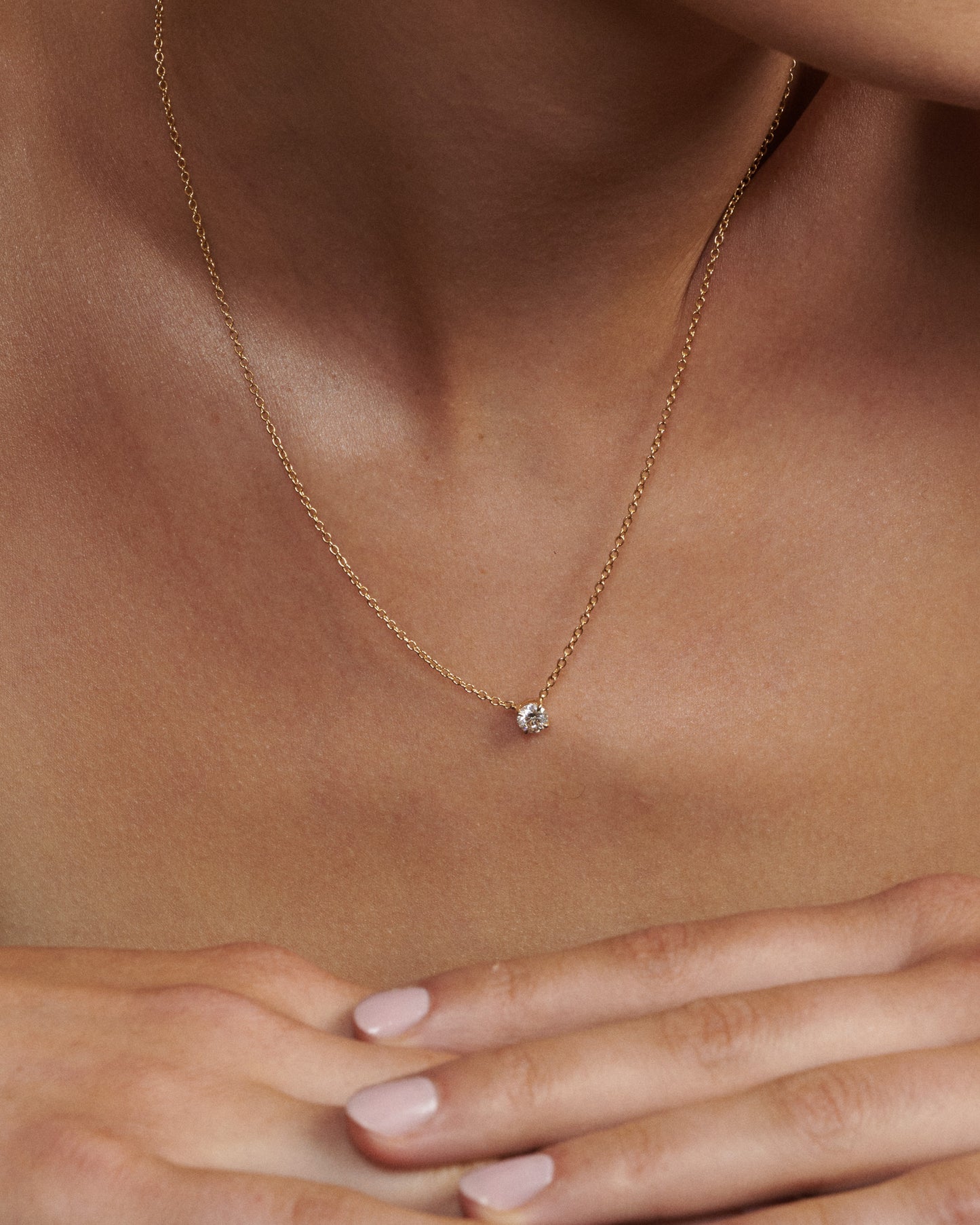 Gold necklace with a small diamond pendant on a person's neck